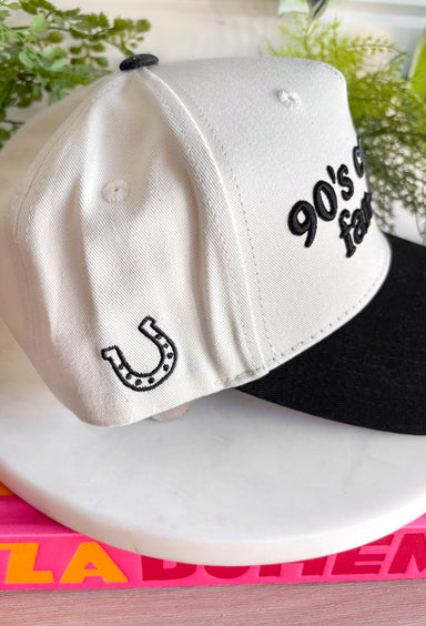 Cue the boot scootin’ playlist! This neutral trucker hat with a bold black bill brings all the throwback country vibes. Featuring “90’s Country Fan Club” across the front and a lucky horseshoe detail on the side, it’s the perfect nod to your favorite era of country music. With its classic trucker silhouette and easy neutral colorway, this hat pairs effortlessly with graphic tees, denim, and cutoffs for that laid-back, off-duty look.
