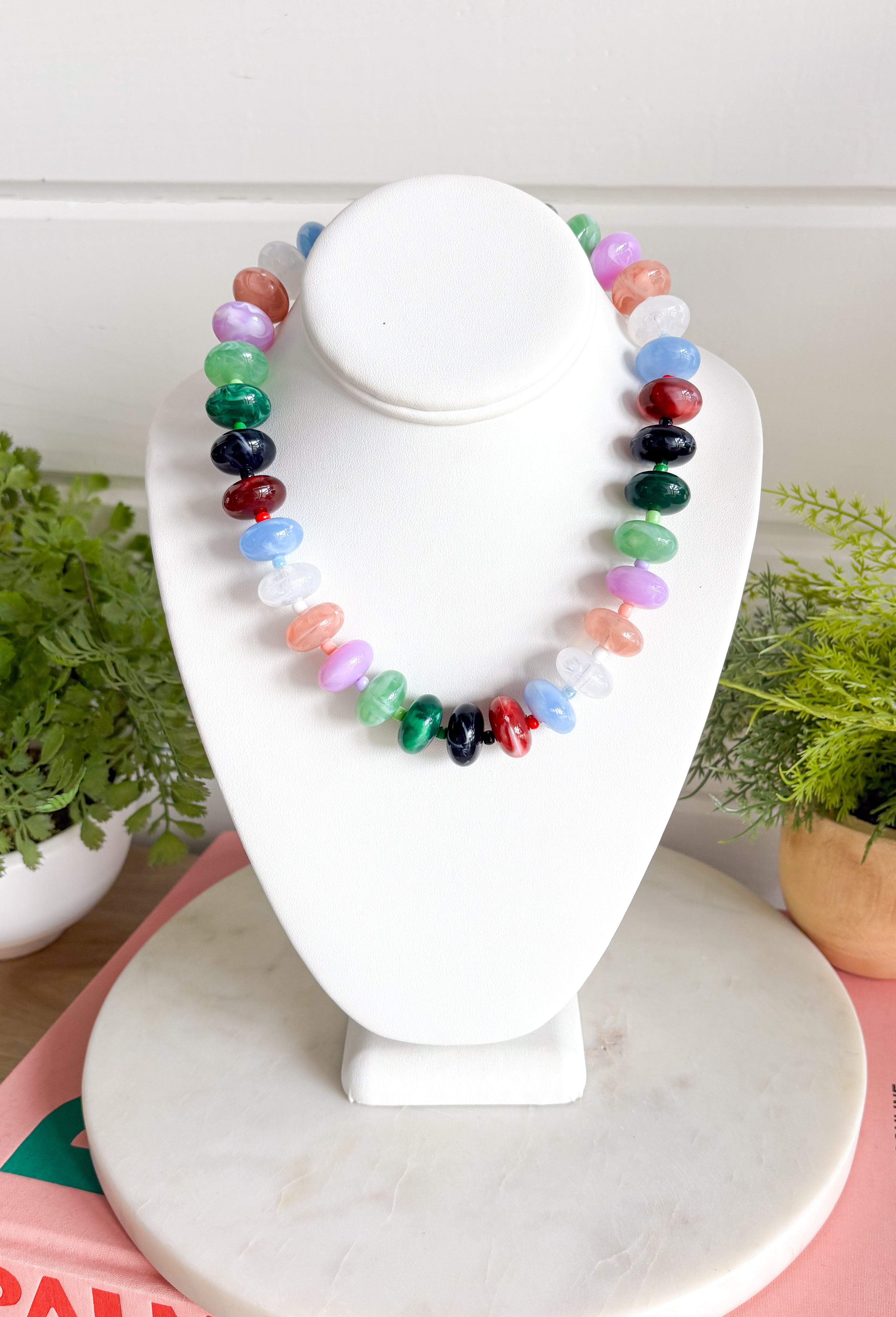 Make a statement with this trendy chunky beaded necklace that's full of color and personality. Featuring bold beads in shades of clear, burgundy, hunter green, green, lilac, blue, and black, this eye-catching accessory is accented with dainty colorful beads between each larger bead for added texture and charm. Whether you're dressing up a simple sweater or adding the finishing touch to your favorite dress, this necklace brings the perfect pop of playful style to any look.