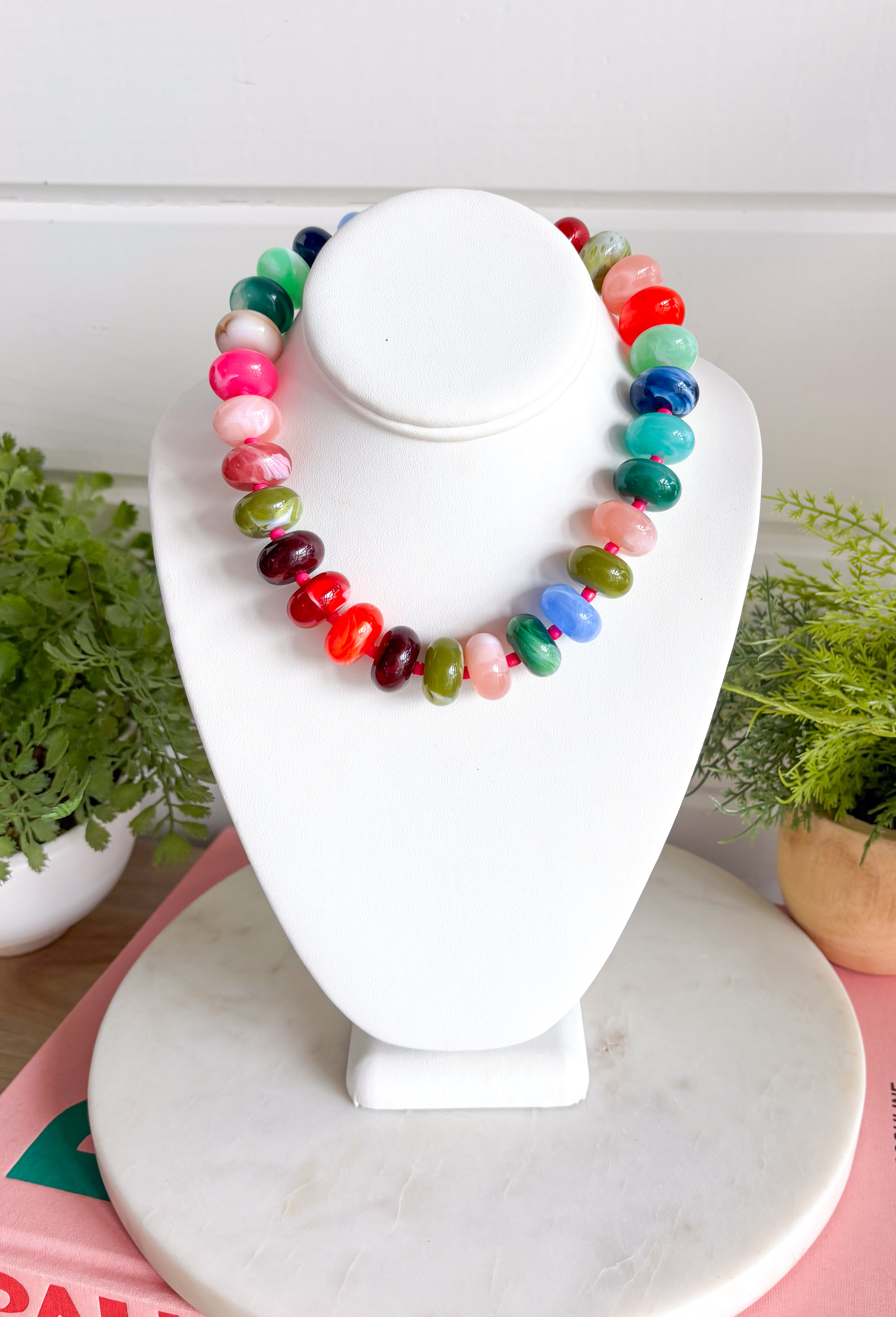 Make a statement with this trendy chunky beaded necklace that's full of color and personality. Featuring bold beads in shades of pink, burgundy, hunter green, green, blue, and black, this eye-catching accessory is accented with dainty colorful pink beads between each larger bead for added texture and charm. Whether you're dressing up a simple sweater or adding the finishing touch to your favorite dress, this necklace brings the perfect pop of playful style to any look.