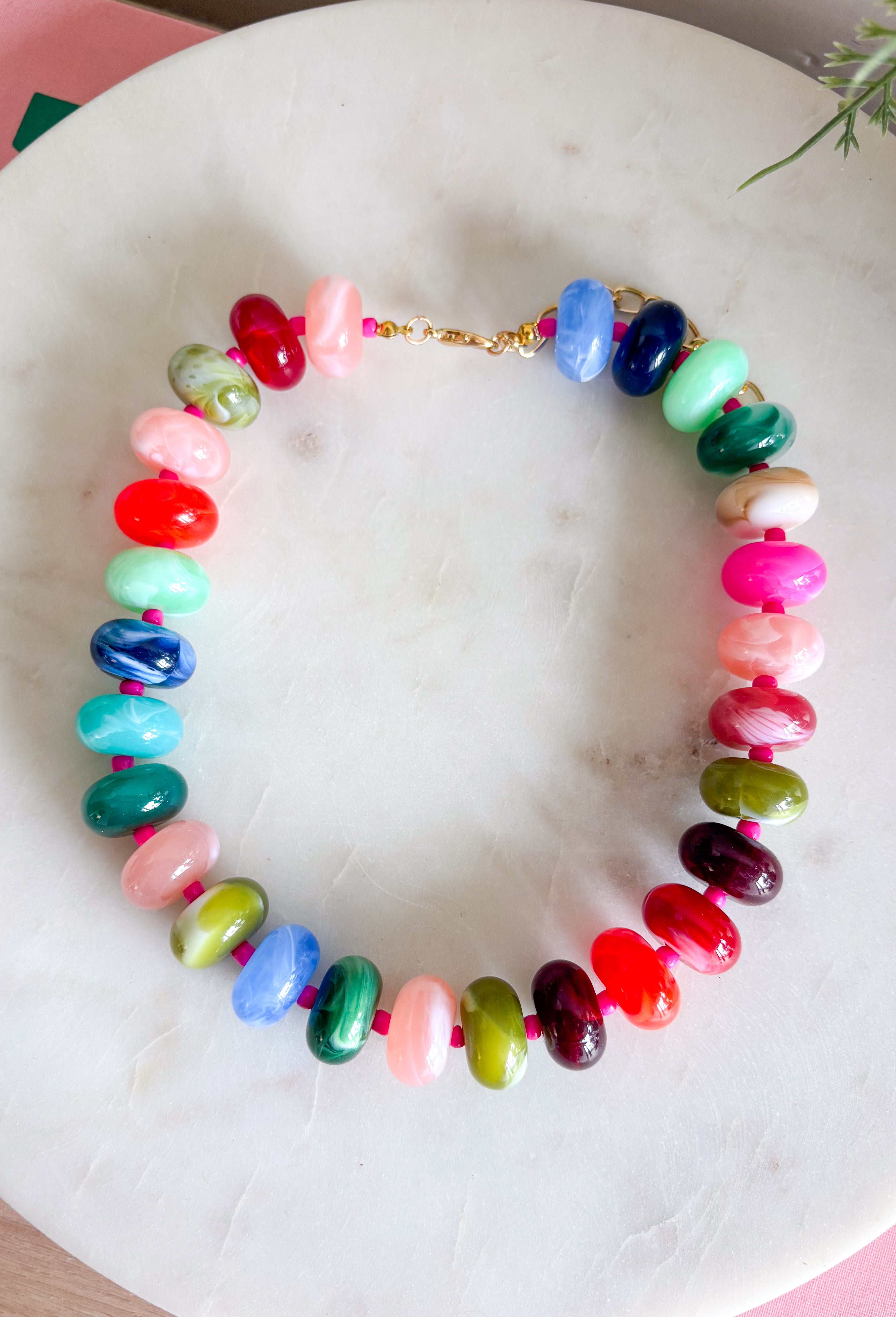 Make a statement with this trendy chunky beaded necklace that's full of color and personality. Featuring bold beads in shades of pink, burgundy, hunter green, green, blue, and black, this eye-catching accessory is accented with dainty colorful pink beads between each larger bead for added texture and charm. Whether you're dressing up a simple sweater or adding the finishing touch to your favorite dress, this necklace brings the perfect pop of playful style to any look.