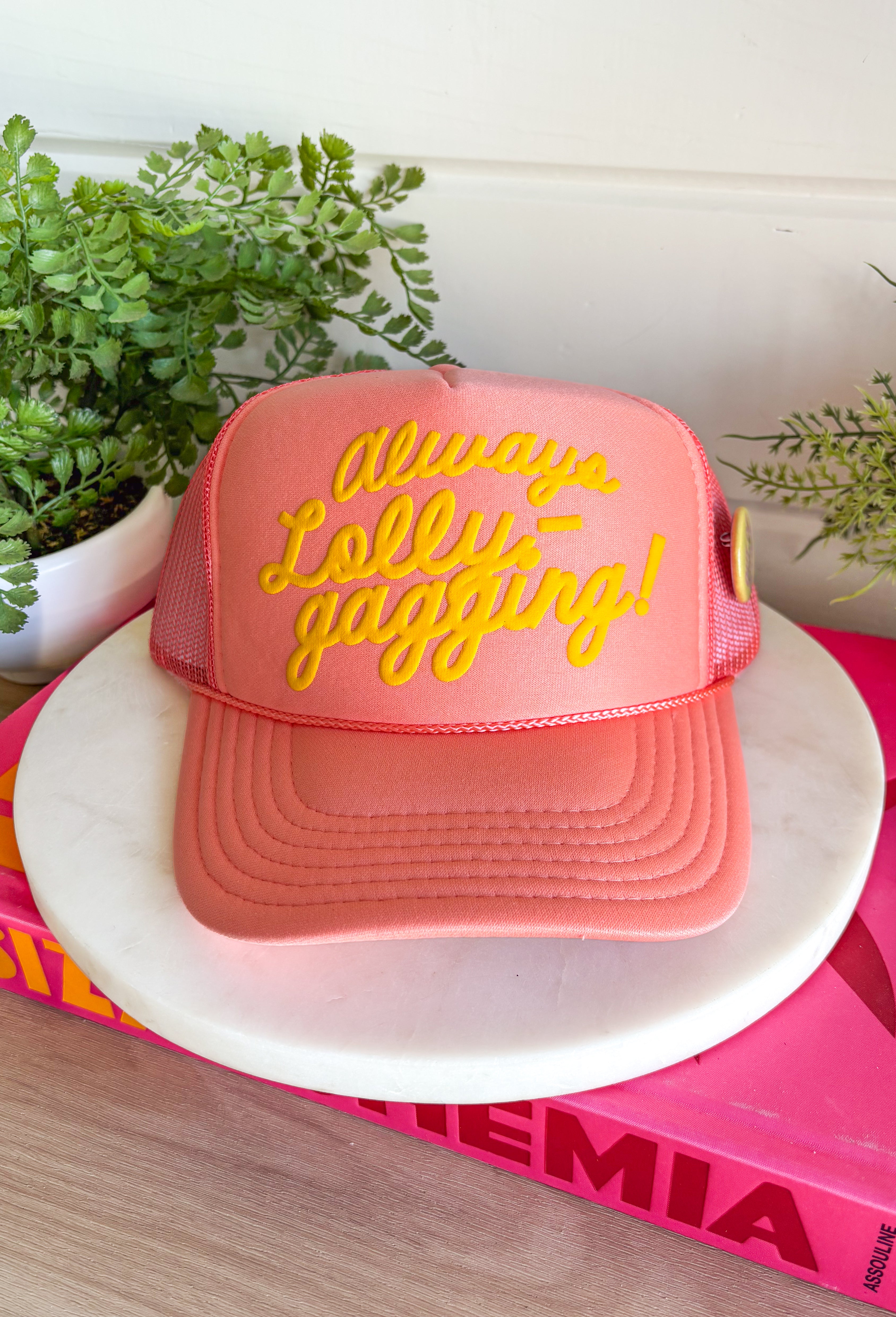 For the girl who’s in no rush and loving it! This coral trucker hat features “Always Lolly-Gagging!” in bright yellow for a fun, carefree statement that doesn’t take life too seriously. Finished with a playful yellow “Sorry Out of Office” button on the side, this hat brings all the laid-back vibes. The breathable mesh backing and adjustable fit make it perfect for sunny days, road trips, and everything in between.