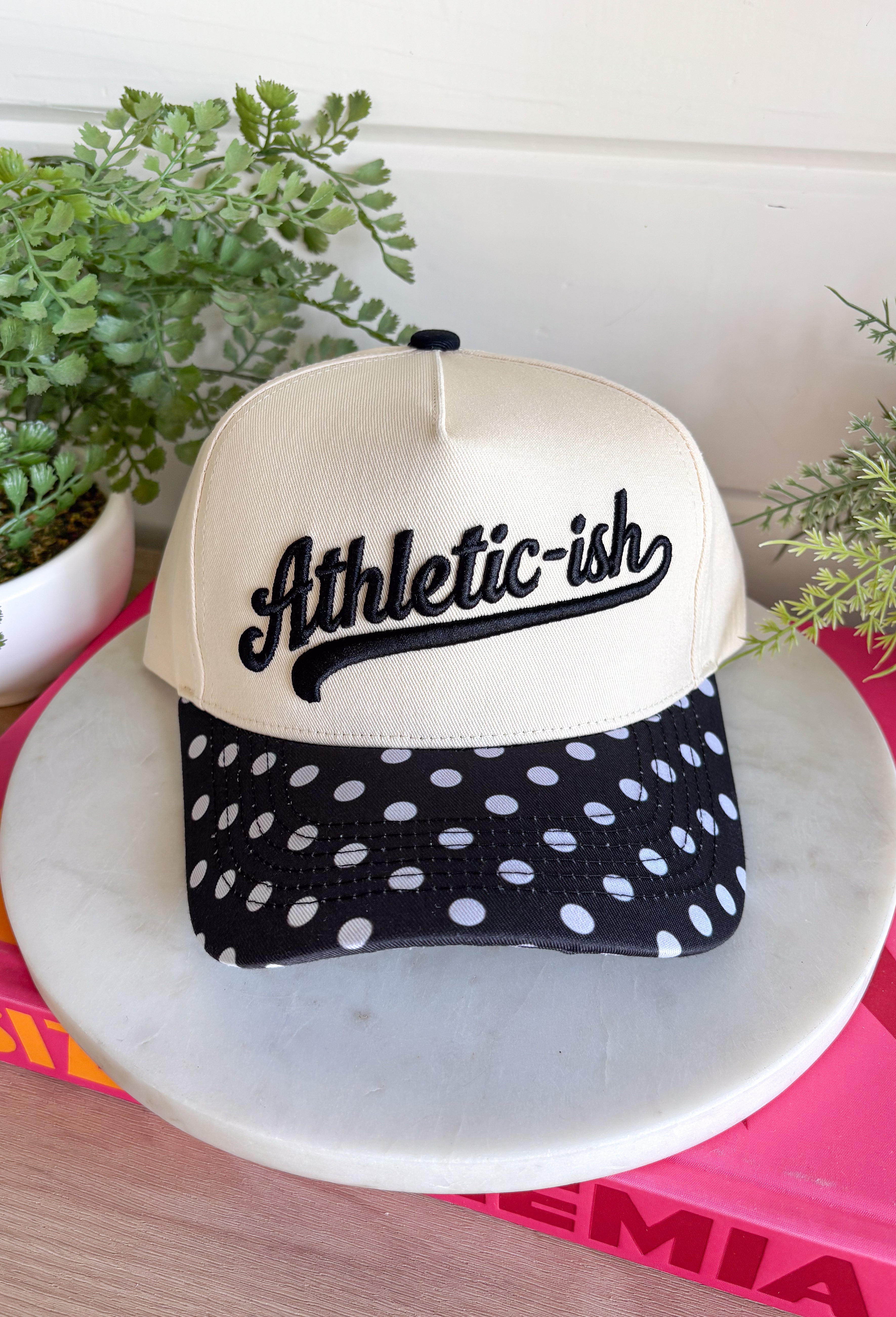 This “Athletic-ish” trucker hat is the perfect mix of cute and a little sarcastic—basically summer energy in one accessory. The neutral base keeps it easy to style, while the black embroidered lettering and polka dot bill add a fun, playful twist. It’s lightweight, breathable, and made for those busy, on-the-go days when you still want to look put together without trying too hard. Whether you're heading to a workout…or just thinking about it, this one gets it. 