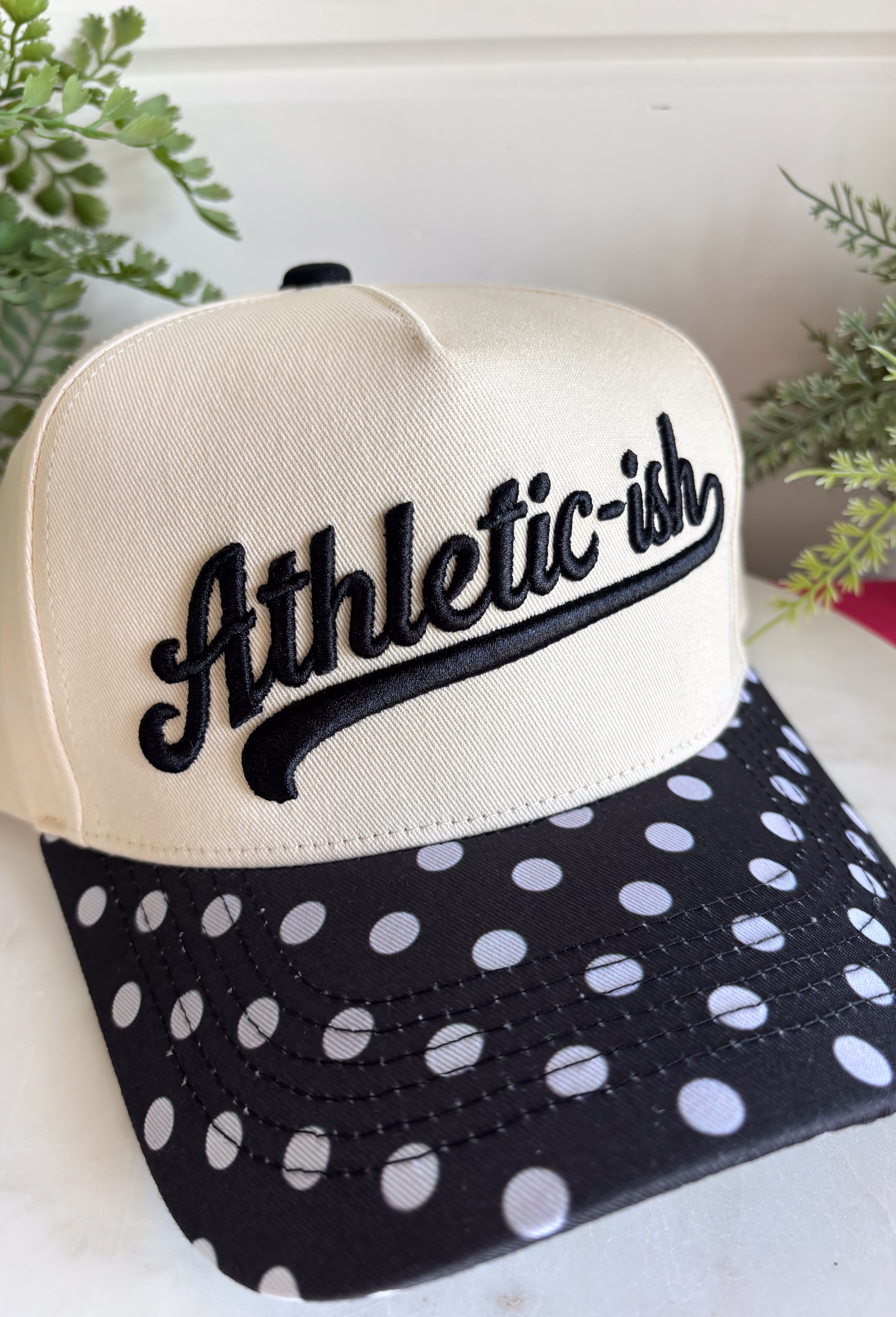 This “Athletic-ish” trucker hat is the perfect mix of cute and a little sarcastic—basically summer energy in one accessory. The neutral base keeps it easy to style, while the black embroidered lettering and polka dot bill add a fun, playful twist. It’s lightweight, breathable, and made for those busy, on-the-go days when you still want to look put together without trying too hard. Whether you're heading to a workout…or just thinking about it, this one gets it.