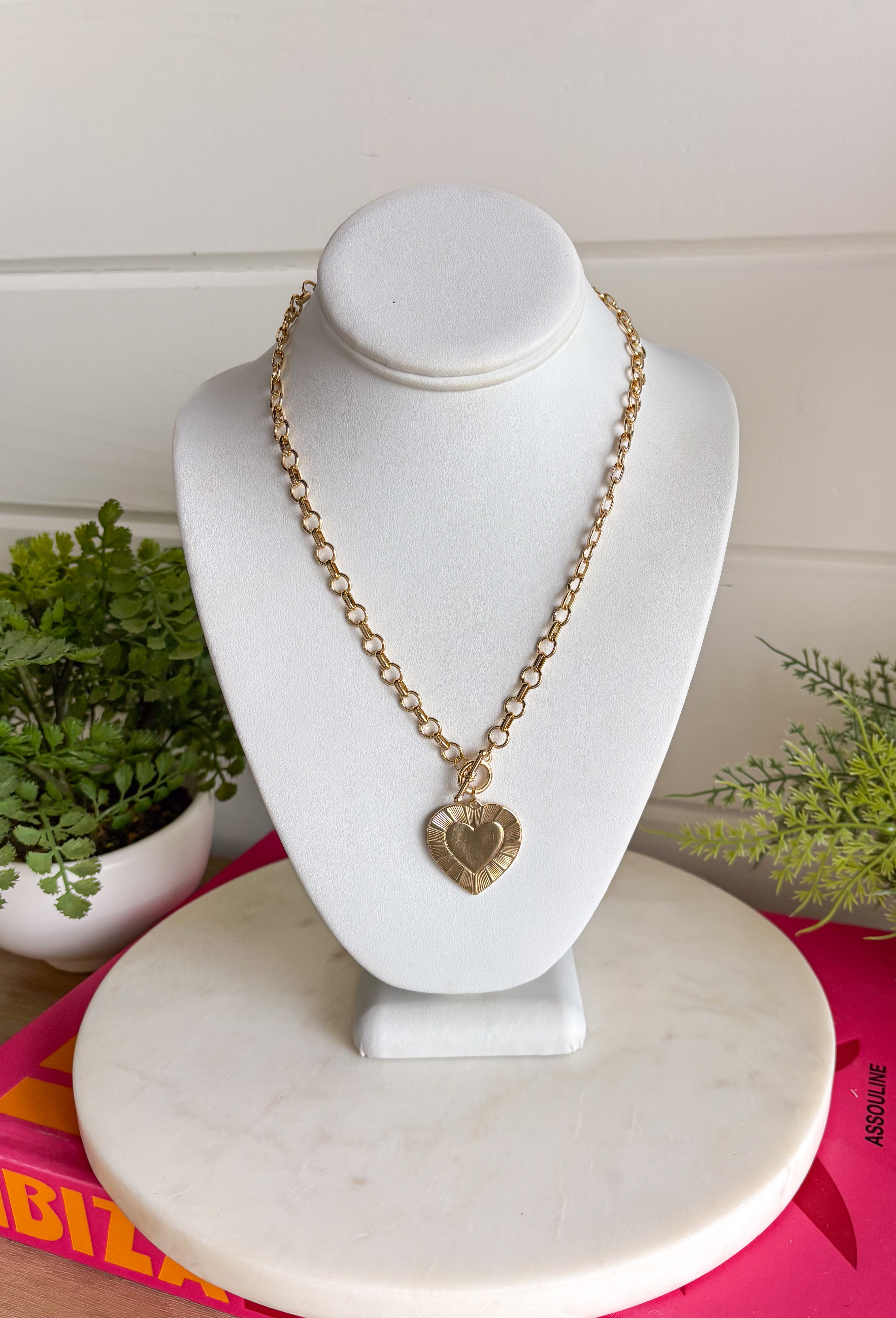 This gold chain necklace with a textured heart pendant is the perfect mix of bold and timeless for styling all season long! The toggle closure adds a unique, elevated touch, while the 18" length makes it ideal for layering or wearing as a statement on its own. The textured heart pendant gives it that eye-catching detail that instantly pulls an outfit together—whether you're in a simple tank or a breezy dress. It’s the kind of piece that feels special but still easy enough for everyday wear. 