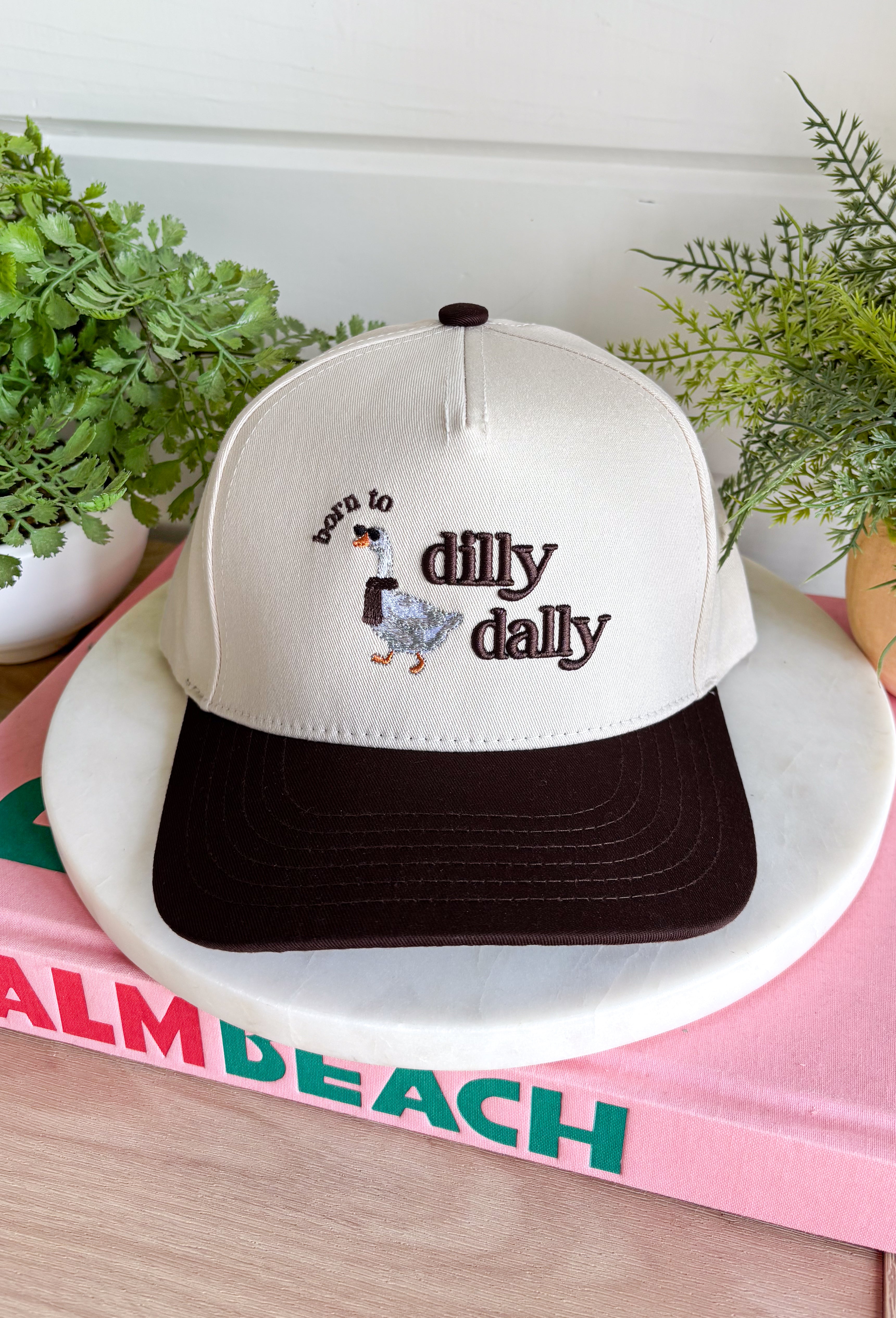 For anyone who considers taking their sweet time a personality trait, this “Born To Dilly Dally” trucker hat from The Happiest gets it. The neutral design is finished with a chocolate brown bill and matching embroidered lettering for an easy, everyday color combo. The real star is the embroidered duck wearing a scarf and sunglasses—because apparently even the ducks have mastered the art of having nowhere important to be.