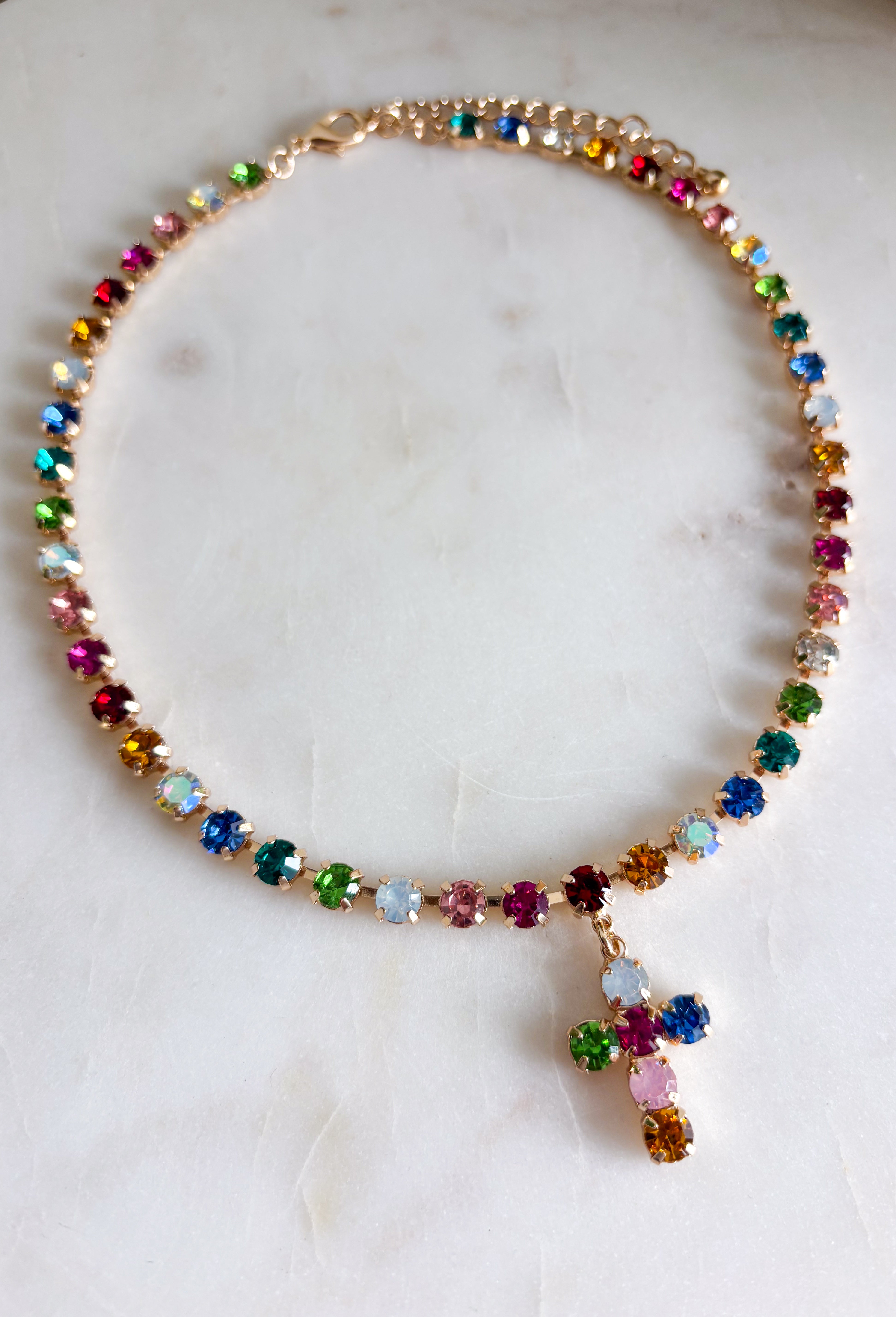 Add a meaningful touch of color to your jewelry collection with this beautiful cross necklace. Featuring a strand of colorful rhinestone crystals in shades of red, blue, green, pink, and gold, this eye-catching piece is finished with a matching cross pendant for the perfect blend of faith and style. The vibrant colors and delicate gold accents make it a standout accessory that's easy to wear for both everyday outfits and special occasions.