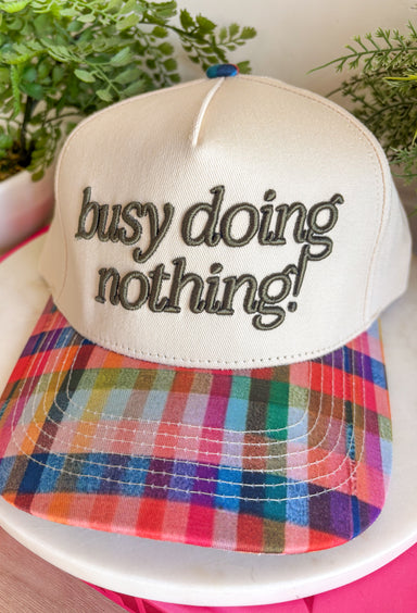 Some days are made for slowing down, and this trucker hat is here for it. Featuring "Busy Doing Nothing" embroidered in a rich deep olive color, it's the perfect accessory for cozy weekends, coffee runs, road trips, and laid-back fall adventures. The colorful plaid bill and matching top button add a fun seasonal touch, giving this hat plenty of personality while keeping it easy to style with your favorite casual outfits. 