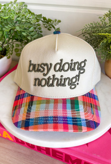 Some days are made for slowing down, and this trucker hat is here for it. Featuring "Busy Doing Nothing" embroidered in a rich deep olive color, it's the perfect accessory for cozy weekends, coffee runs, road trips, and laid-back fall adventures. The colorful plaid bill and matching top button add a fun seasonal touch, giving this hat plenty of personality while keeping it easy to style with your favorite casual outfits. 