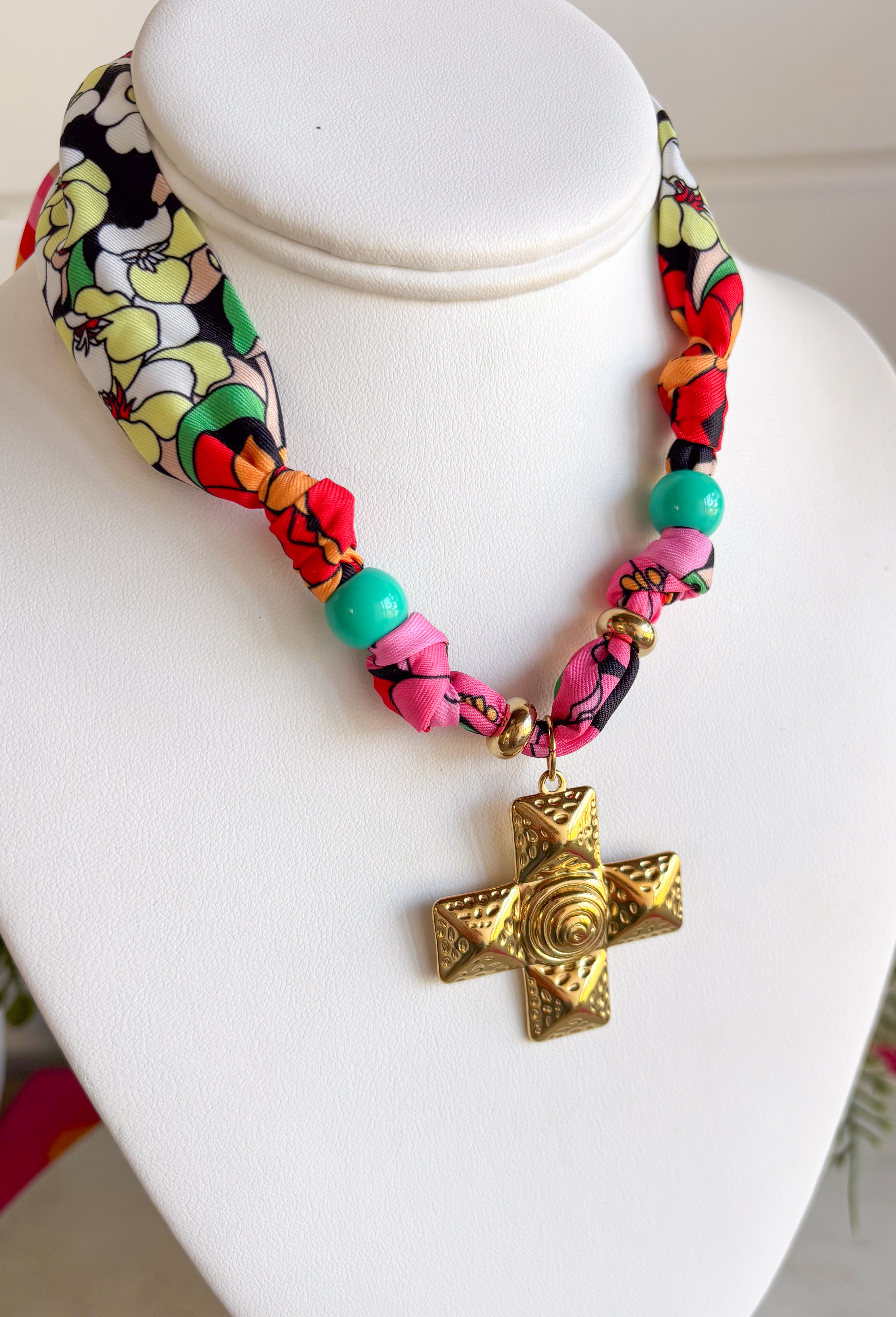 A little bold, a little western, and full of personality! This colorful bandana scarf necklace blends vibrant prints with meaningful details for a statement accessory you’ll love wearing. The scarf features black and white florals paired with bright stripes in pink, green, red, orange, and yellow for a fun pop of color. Finished with a gold textured cross pendant and a turquoise bead accent, this piece brings together playful style with a hint of western charm. 