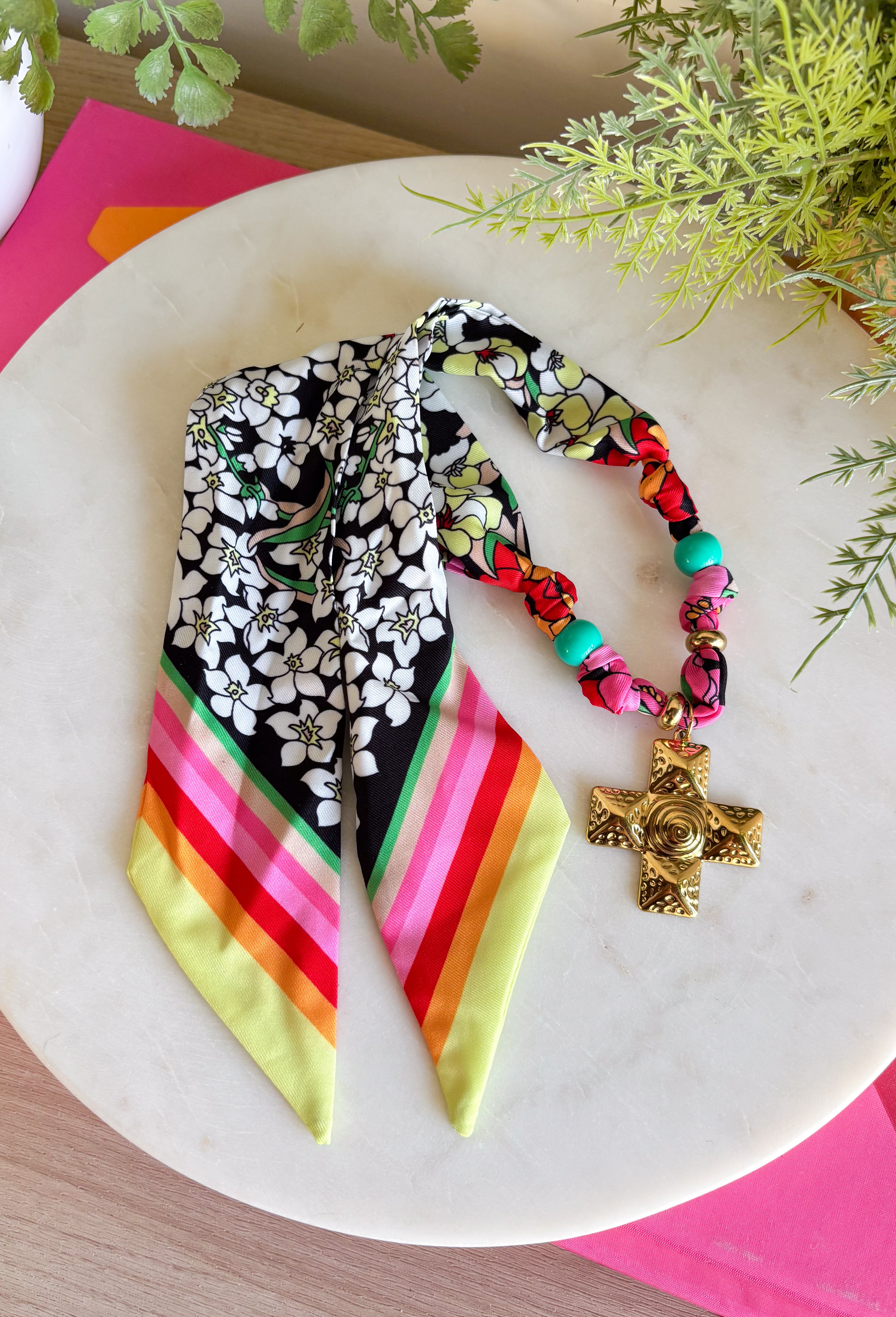 A little bold, a little western, and full of personality! This colorful bandana scarf necklace blends vibrant prints with meaningful details for a statement accessory you’ll love wearing. The scarf features black and white florals paired with bright stripes in pink, green, red, orange, and yellow for a fun pop of color. Finished with a gold textured cross pendant and a turquoise bead accent, this piece brings together playful style with a hint of western charm. 