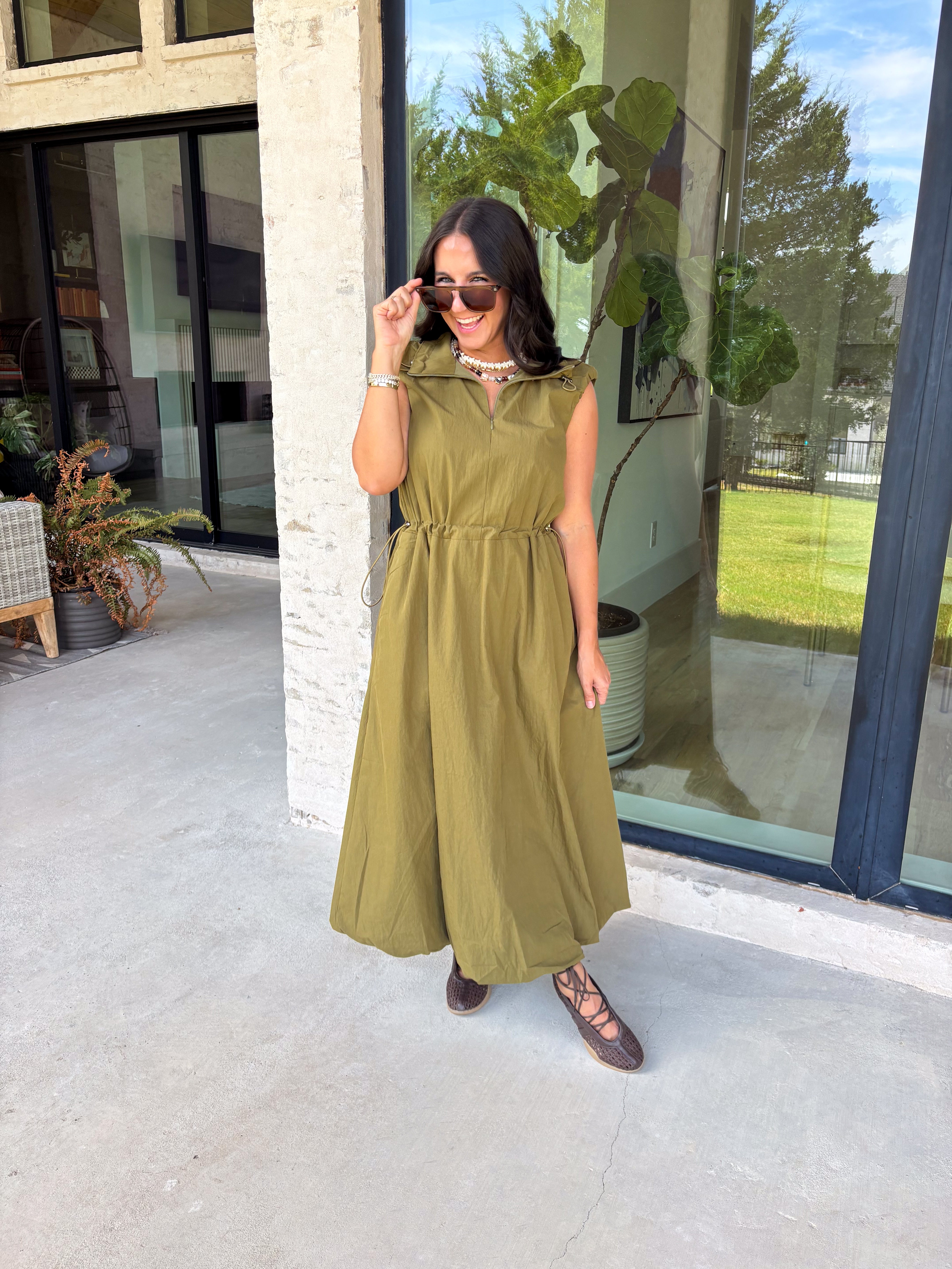 Meet your new throw-on-and-go favorite with this olive utility-inspired midi dress from Entro. The classic olive color keeps it versatile, while the zipper-front closure and adjustable waist give it a sporty, modern feel. A bubble hem adds shape and a fun unexpected finish, while the sleeveless silhouette makes it easy to wear now and layer as the temperatures cool down. Complete with convenient side pockets, this dress is ready for busy workdays, weekend plans, travel days, and everything in between.