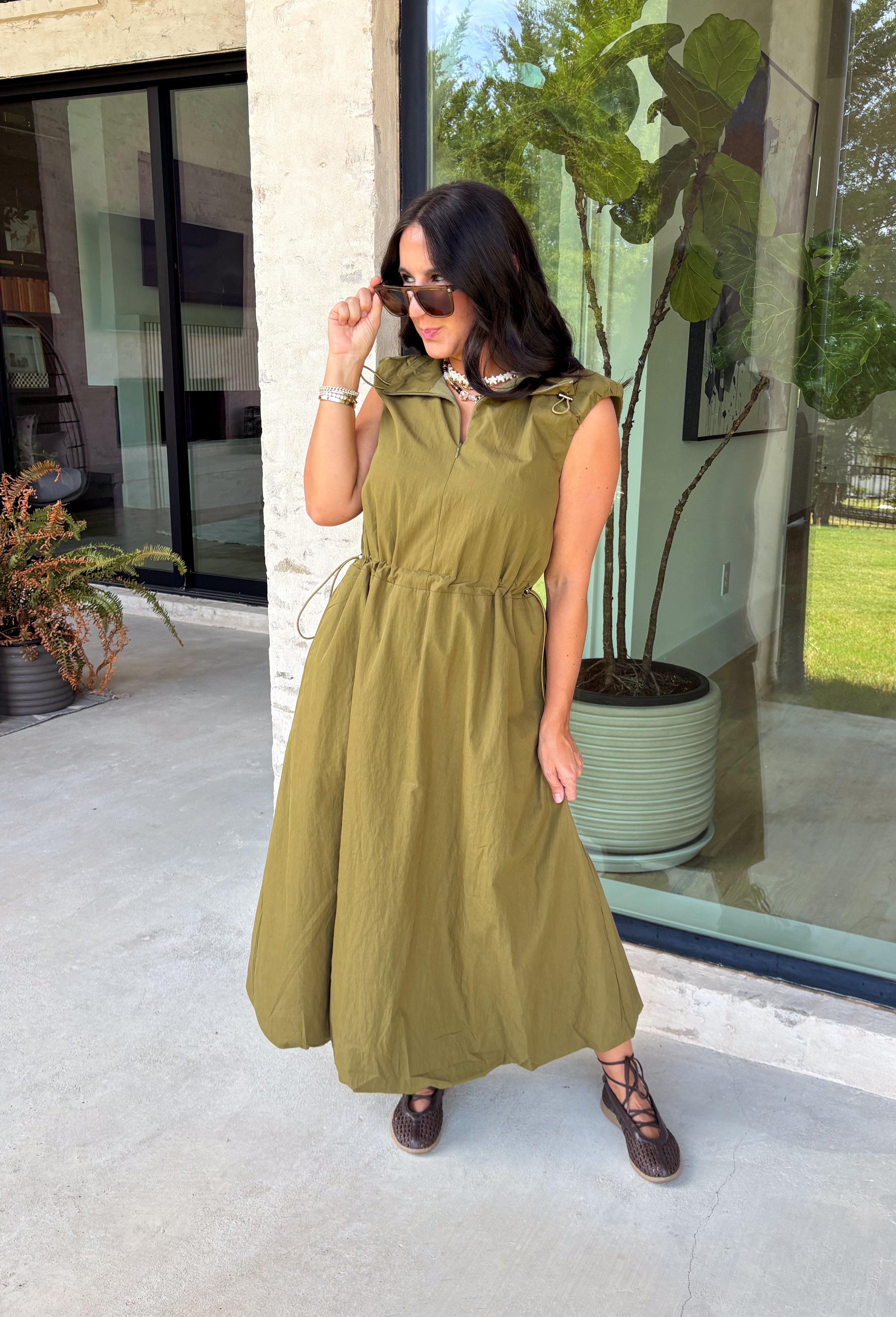Meet your new throw-on-and-go favorite with this olive utility-inspired midi dress from Entro. The classic olive color keeps it versatile, while the zipper-front closure and adjustable waist give it a sporty, modern feel. A bubble hem adds shape and a fun unexpected finish, while the sleeveless silhouette makes it easy to wear now and layer as the temperatures cool down. Complete with convenient side pockets, this dress is ready for busy workdays, weekend plans, travel days, and everything in between.