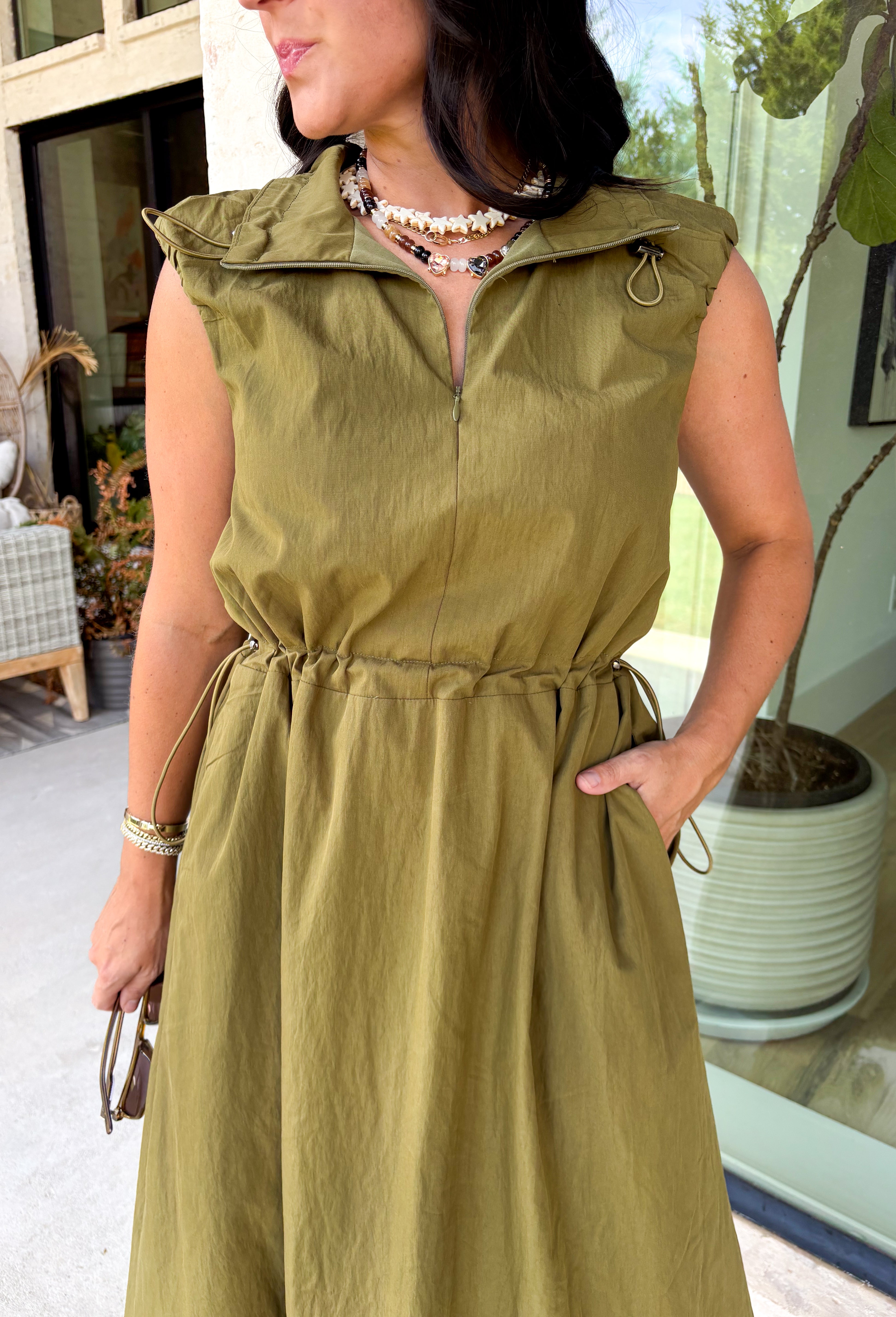 Meet your new throw-on-and-go favorite with this olive utility-inspired midi dress from Entro. The classic olive color keeps it versatile, while the zipper-front closure and adjustable waist give it a sporty, modern feel. A bubble hem adds shape and a fun unexpected finish, while the sleeveless silhouette makes it easy to wear now and layer as the temperatures cool down. Complete with convenient side pockets, this dress is ready for busy workdays, weekend plans, travel days, and everything in between.
