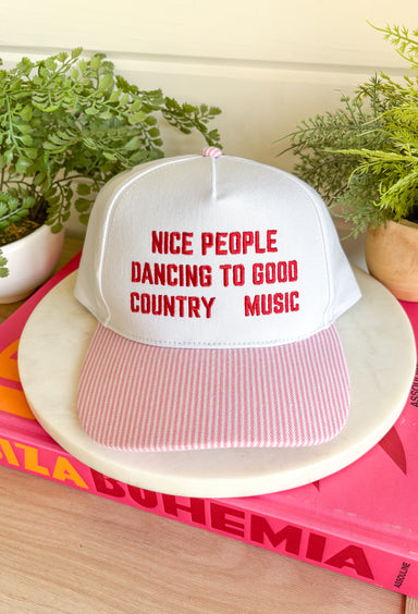 Cue the country playlist—this trucker hat was made for good times and great company! Featuring&nbsp;"Nice People Dancing To Good Country Music" embroidered across the front in bold red stitching, this playful hat is perfect for concerts, tailgates, rodeos, and weekends spent outdoors. The pink and white striped bill adds a fun pop of color, while the matching top button ties the look together. Finished with an adjustable fit, it's the perfect accessory for every country music lover.