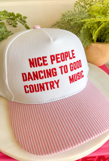 Cue the country playlist—this trucker hat was made for good times and great company! Featuring&nbsp;"Nice People Dancing To Good Country Music" embroidered across the front in bold red stitching, this playful hat is perfect for concerts, tailgates, rodeos, and weekends spent outdoors. The pink and white striped bill adds a fun pop of color, while the matching top button ties the look together. Finished with an adjustable fit, it's the perfect accessory for every country music lover.
