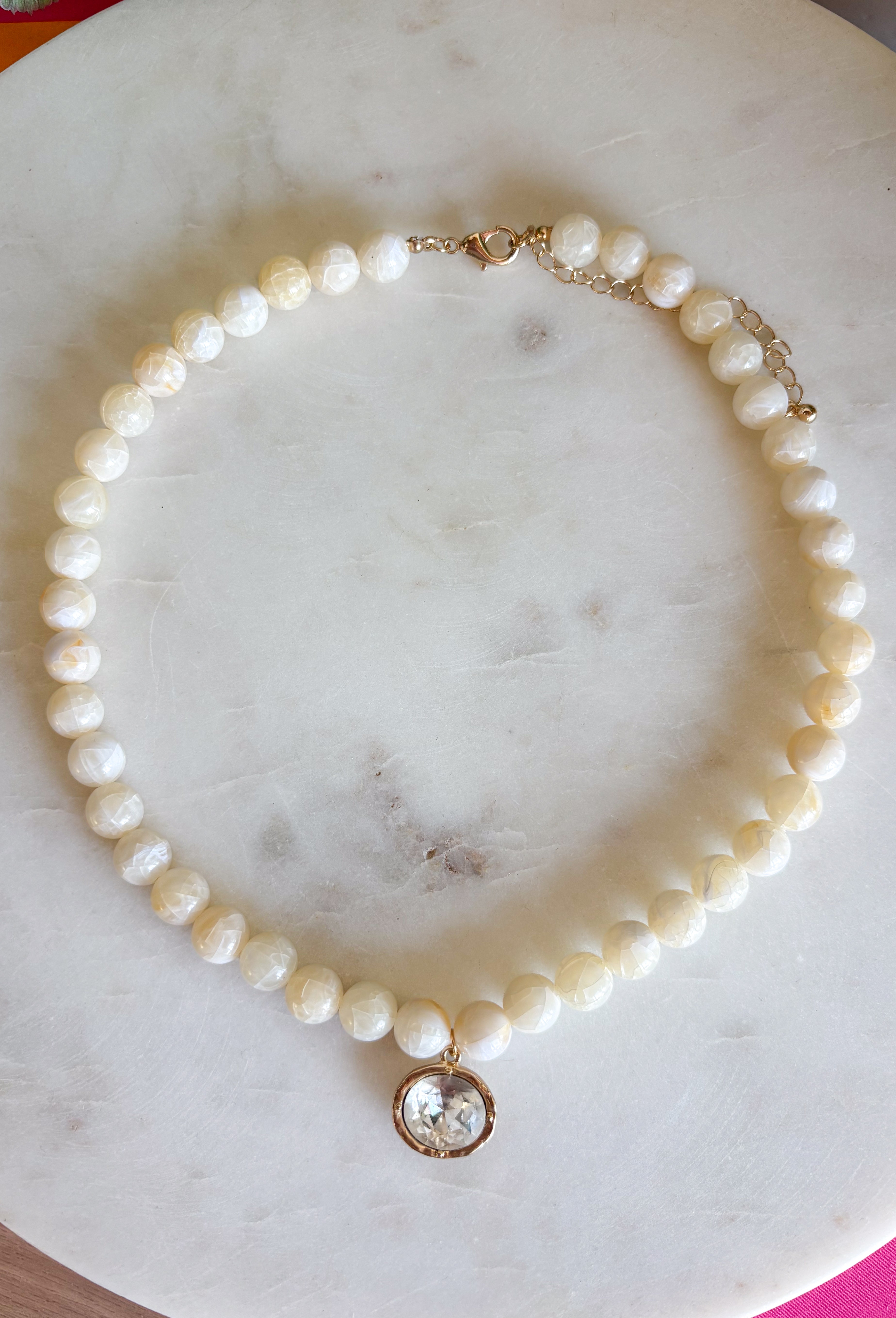 Elegant, timeless, and effortlessly versatile, this ivory beaded necklace is the perfect accessory to elevate any outfit. Featuring beautiful ivory beads, this classic piece is accented with a dazzling crystal rhinestone charm that adds just the right amount of shimmer. Whether you're dressing up a cozy sweater, styling your favorite blouse, or adding a polished finishing touch to a special occasion look, this necklace is one you'll reach for season after season.