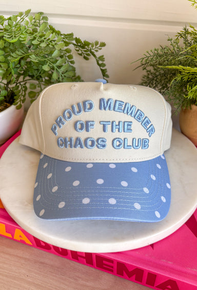 Wear your badge of honor with a smile in this playful trucker hat. Featuring "Proud Member Of The Chaos Club" embroidered in a classic denim blue, this hat is made for busy days, endless to-do lists, and embracing every bit of the fun along the way. The denim blue bill with an off white polka dot print adds a charming vintage-inspired touch, making it the perfect accessory for school drop-offs, errands, weekend adventures, and everything in between.
