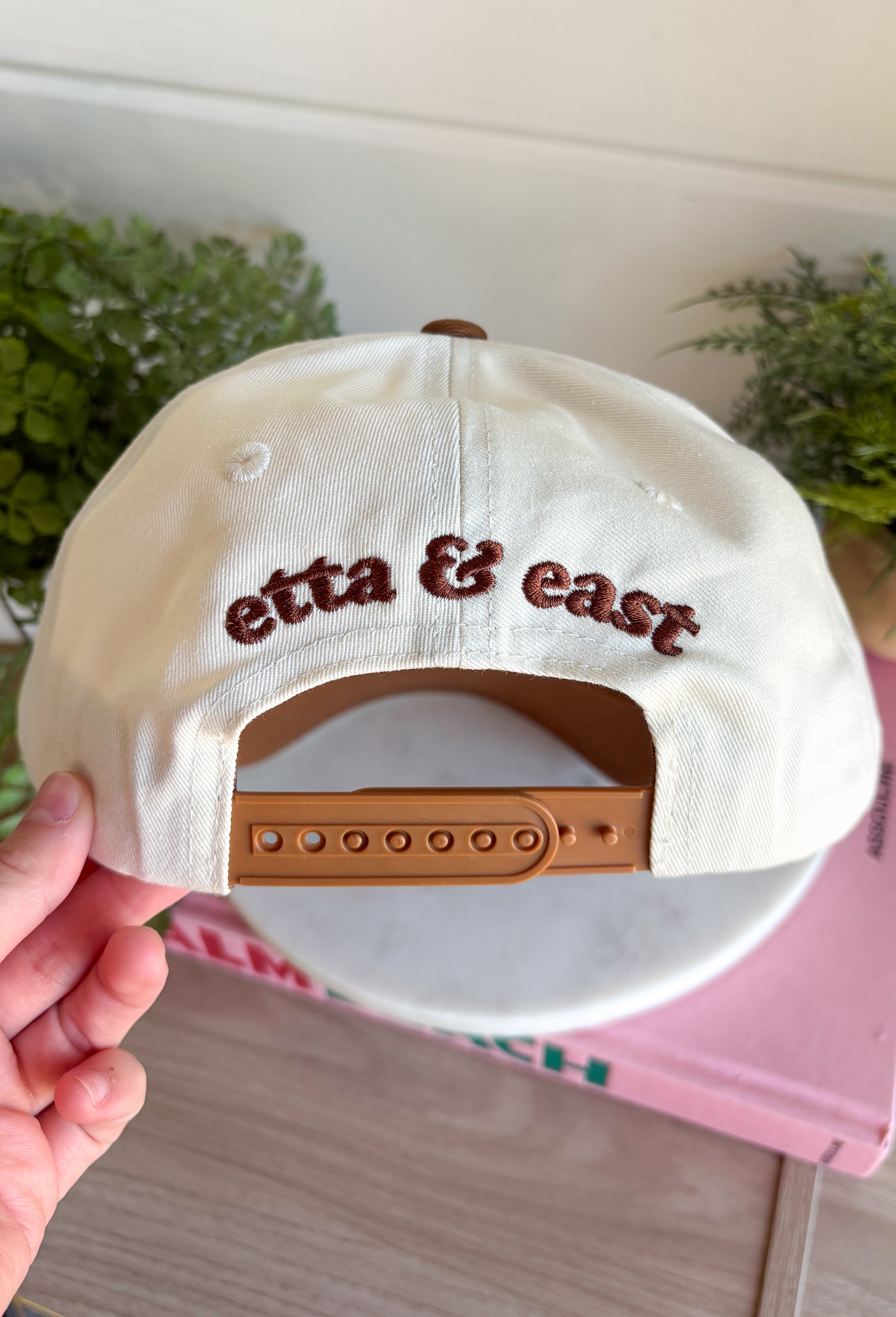 A little reminder to appreciate the good stuff! This neutral trucker hat from Etta &amp; East features colorful embroidered “How Lucky Are We” lettering across the front for a playful pop against the classic neutral design. A rich brown bill gives it an autumn-ready feel, while an embroidered horseshoe on the side adds an extra lucky touch. Finished with an adjustable fit, it’s an easy grab-and-go accessory for football weekends, coffee runs, road trips, and everyday errands.