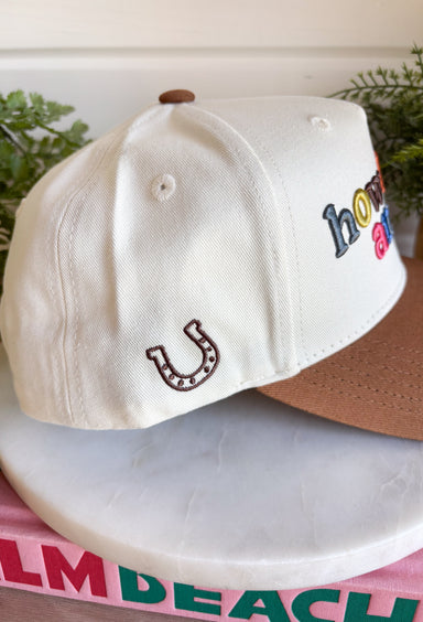 A little reminder to appreciate the good stuff! This neutral trucker hat from Etta &amp; East features colorful embroidered “How Lucky Are We” lettering across the front for a playful pop against the classic neutral design. A rich brown bill gives it an autumn-ready feel, while an embroidered horseshoe on the side adds an extra lucky touch. Finished with an adjustable fit, it’s an easy grab-and-go accessory for football weekends, coffee runs, road trips, and everyday errands.