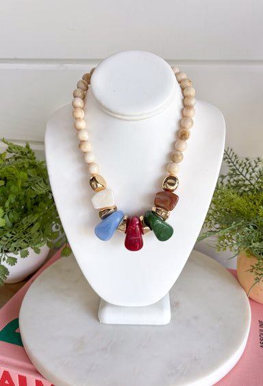 Neutral meets statement-making color with this eye-catching beaded necklace. A neutral beaded strand is accented with larger stone details across the front in rich brown, olive, fuchsia, and light blue, creating a playful mix of earthy and colorful tones. Gold beading between the stones adds a touch of shine and helps each color stand out. It’s the perfect piece when you want an accessory that’s easy to wear but still brings something extra to your outfit.