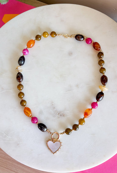 Rich autumn tones and elegant details come together in this stunning statement necklace. Featuring shades of brown with beautiful pops of pink and rust, this beaded design is accented with delicate gold spacer beads that add the perfect touch of shine. The mother-of-pearl heart pendant framed in gold creates a timeless focal point, while the toggle detail and lobster clasp complete this effortlessly elevated accessory. It's the perfect finishing touch for all your favorite fall looks.