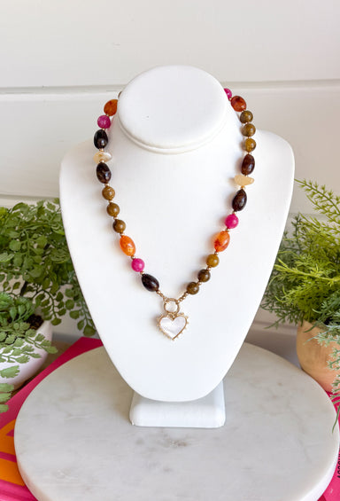 Rich autumn tones and elegant details come together in this stunning statement necklace. Featuring shades of brown with beautiful pops of pink and rust, this beaded design is accented with delicate gold spacer beads that add the perfect touch of shine. The mother-of-pearl heart pendant framed in gold creates a timeless focal point, while the toggle detail and lobster clasp complete this effortlessly elevated accessory. It's the perfect finishing touch for all your favorite fall looks.