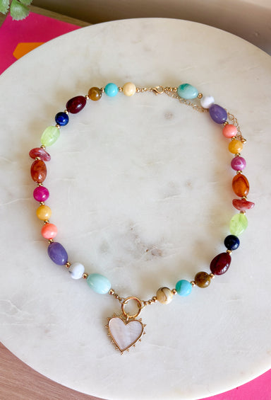 Rich autumn tones and elegant details come together in this stunning statement necklace. Featuring shades of brown with beautiful pops of pink, teal, green, purple, and rust, this beaded design is accented with delicate gold spacer beads that add the perfect touch of shine. The mother-of-pearl heart pendant framed in gold creates a timeless focal point, while the toggle detail and lobster clasp complete this effortlessly elevated accessory. It's the perfect finishing touch for all your favorite fall looks.