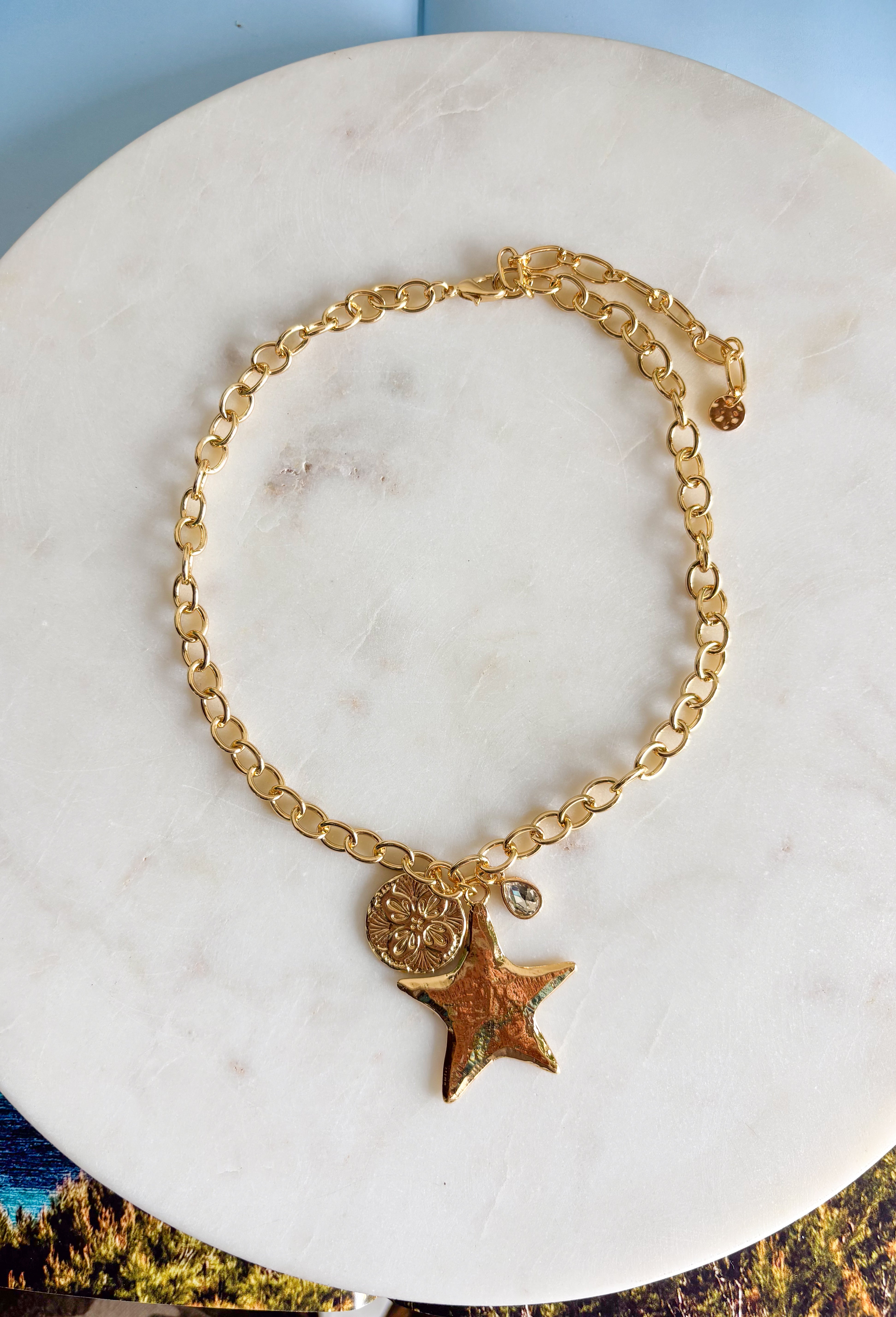 A little sparkle with a playful star detail! This gold open chain necklace features a textured star pendant paired with a textured circle charm and a delicate crystal accent for the perfect hint of shine. The layered charm design adds dimension and personality while still feeling effortless and easy to wear. Trendy yet timeless, this piece looks beautiful worn on its own or layered with your favorite gold necklaces. 