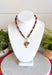 Rich earthy tones and meaningful details come together beautifully in this charm necklace that's perfect for the fall season. Featuring warm brown beads, this eye-catching piece is adorned with a mix of charms, including a gold cross, a natural brown stone, a sparkling brown crystal, and hammered gold accents for added texture and shine. Whether worn with a cozy sweater or your favorite dress, this unique necklace adds effortless charm and personality to every outfit.