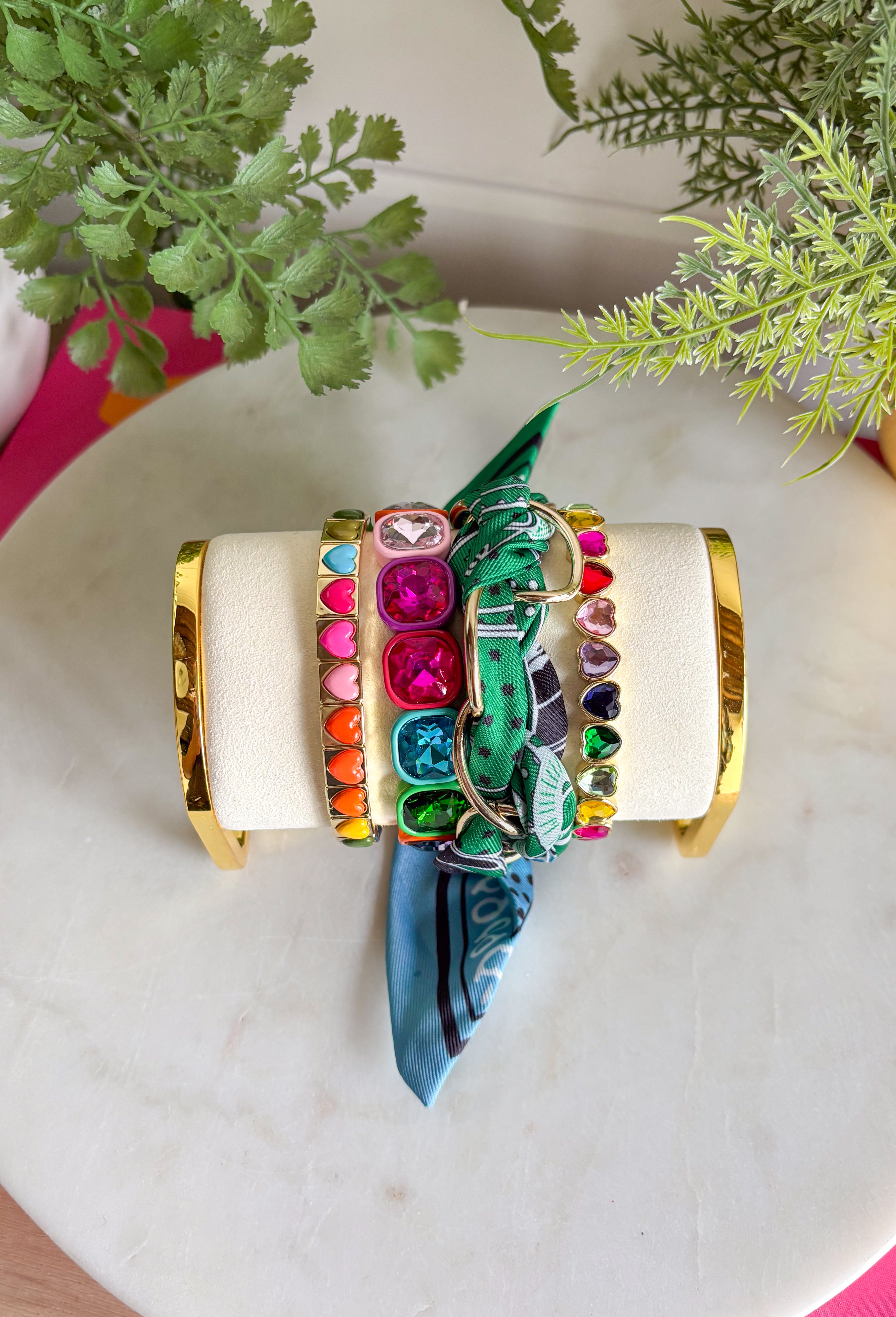 A bold accessory with a cool, laid-back vibe! This fabric wrapped chain link bracelet features oversized gold chain links wrapped in a silky bandana-style fabric. The mix of green and blue tones with pops of black and white creates a fun, eye-catching look that feels both stylish and effortless. The contrast between the polished gold chain and the soft patterned fabric gives this bracelet a unique statement feel. 