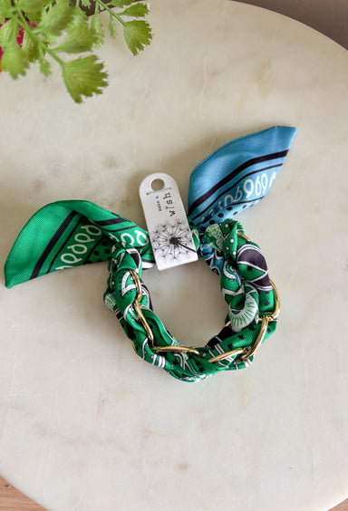 A bold accessory with a cool, laid-back vibe! This fabric wrapped chain link bracelet features oversized gold chain links wrapped in a silky bandana-style fabric. The mix of green and blue tones with pops of black and white creates a fun, eye-catching look that feels both stylish and effortless. The contrast between the polished gold chain and the soft patterned fabric gives this bracelet a unique statement feel. 