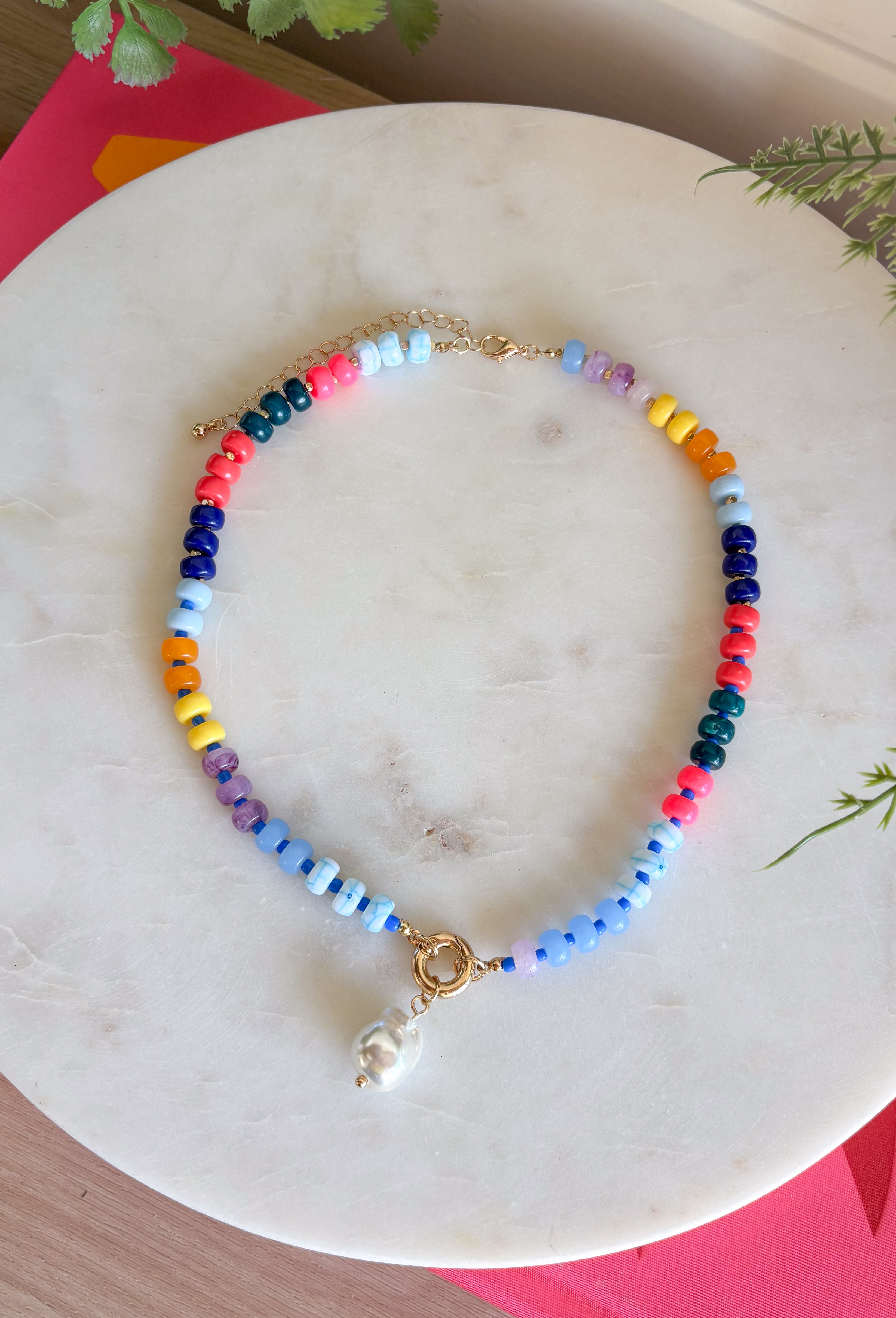 This colorful beaded necklace is the perfect accessory for adding a playful pop to your summer style! Featuring vibrant beads, a chic gold toggle clasp, and a pearl pendant charm, it combines trendy details with a timeless touch. The mix of color and pearl accents creates a fun, elevated look that's easy to wear with everything from casual tanks to breezy dresses. Whether you're heading on vacation, brunch with friends, or simply brightening up an everyday outfit, this necklace is sure to become a favorite.