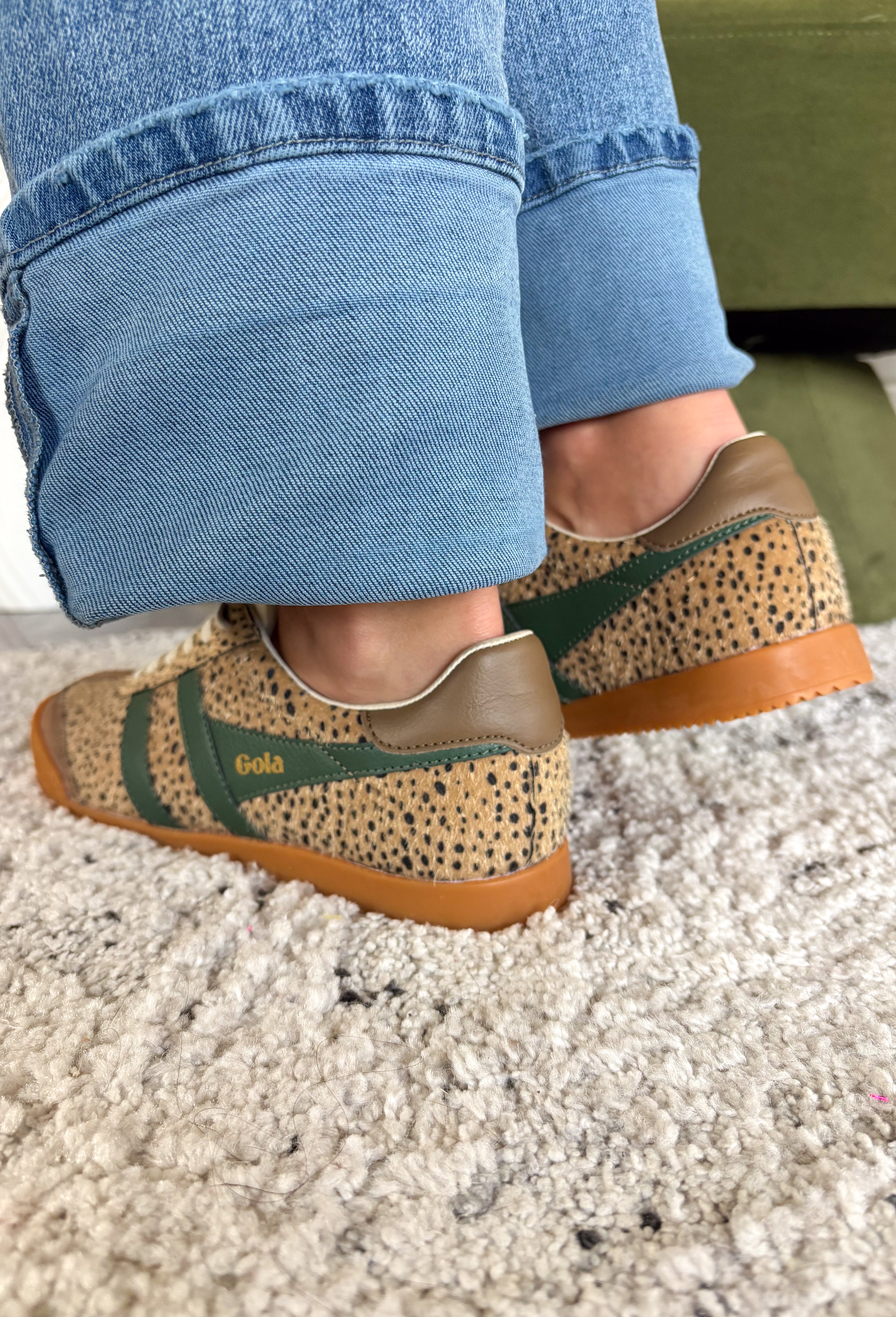 A person wearing cuffed blue jeans and leopard-patterned low-top sneakers with green side stripes