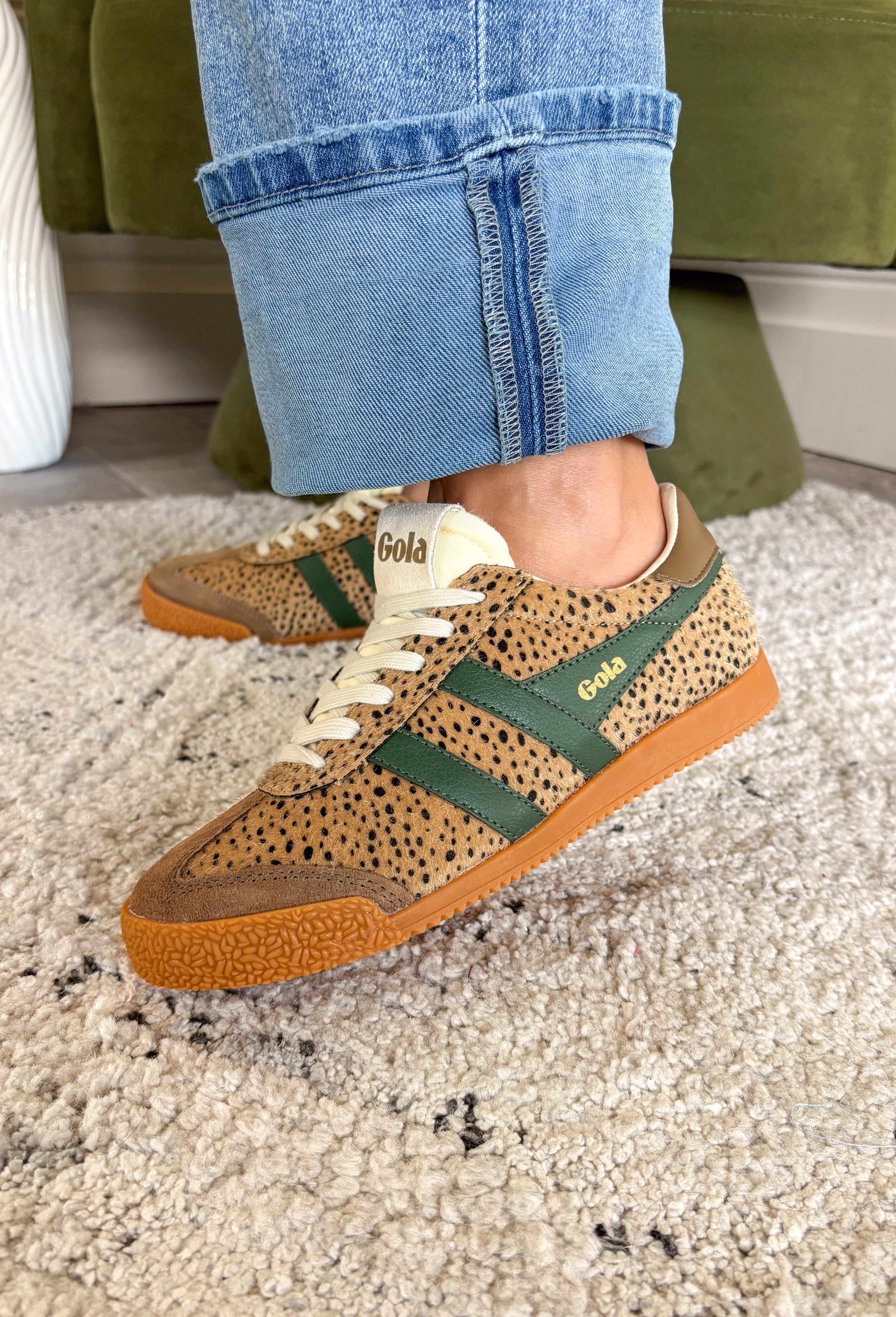 A person wearing cuffed blue jeans and leopard-patterned low-top sneakers with green side stripes