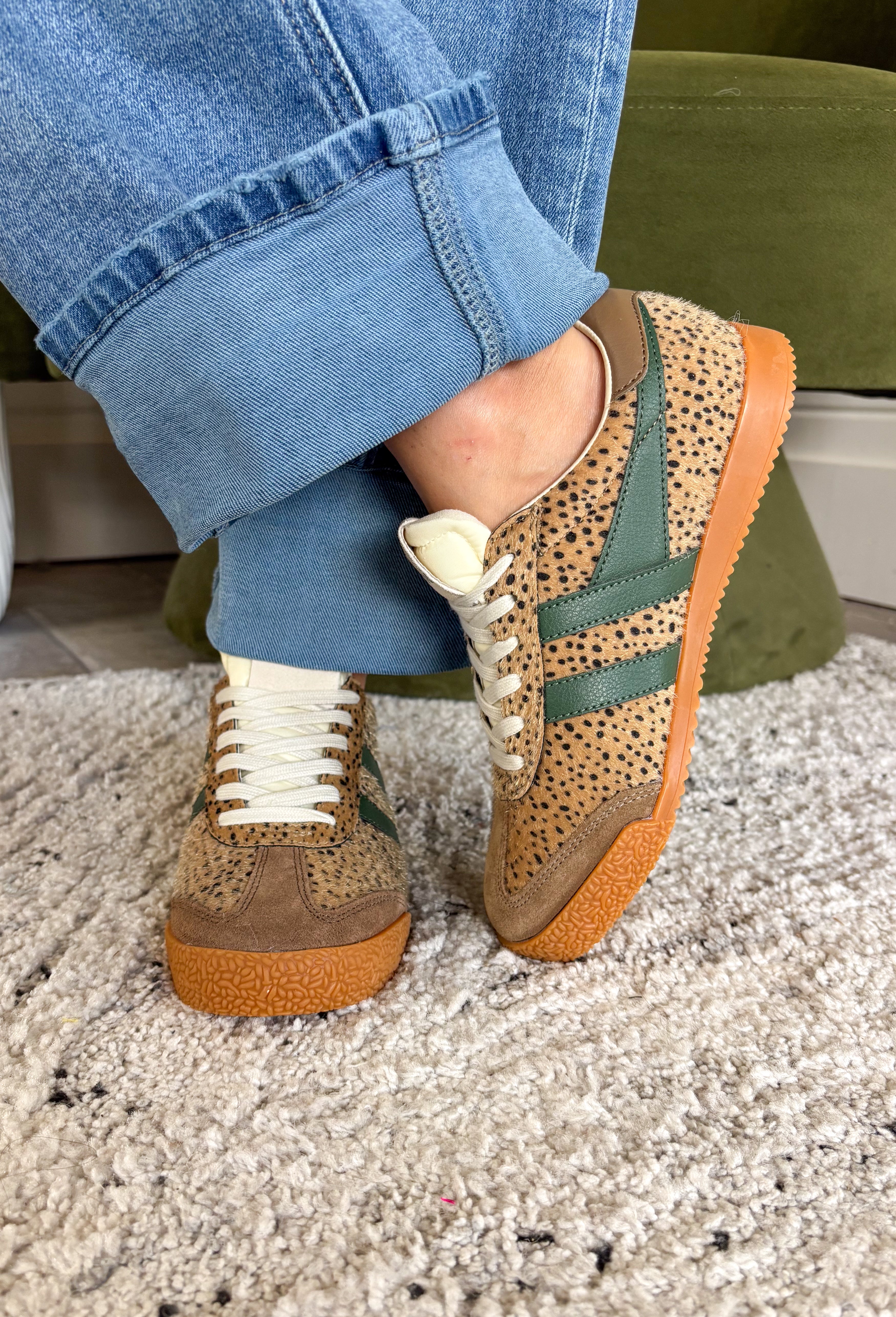 A person wearing cuffed blue jeans and leopard-patterned low-top sneakers with green side stripes