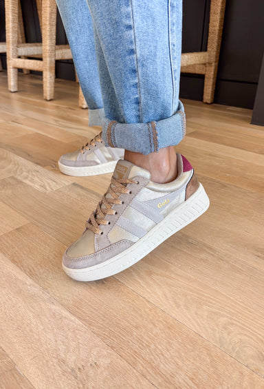 Step into seasonal style with this fresh take on a classic Gola sneaker. Muted gold tones set the stage, while off-white and cerise accents add the perfect pop of contrast. Designed for all-day comfort and everyday wear, this sneaker blends retro charm with modern versatility. Whether paired with denim, dresses, or athleisure, it’s a go-to choice that works across the seasons.