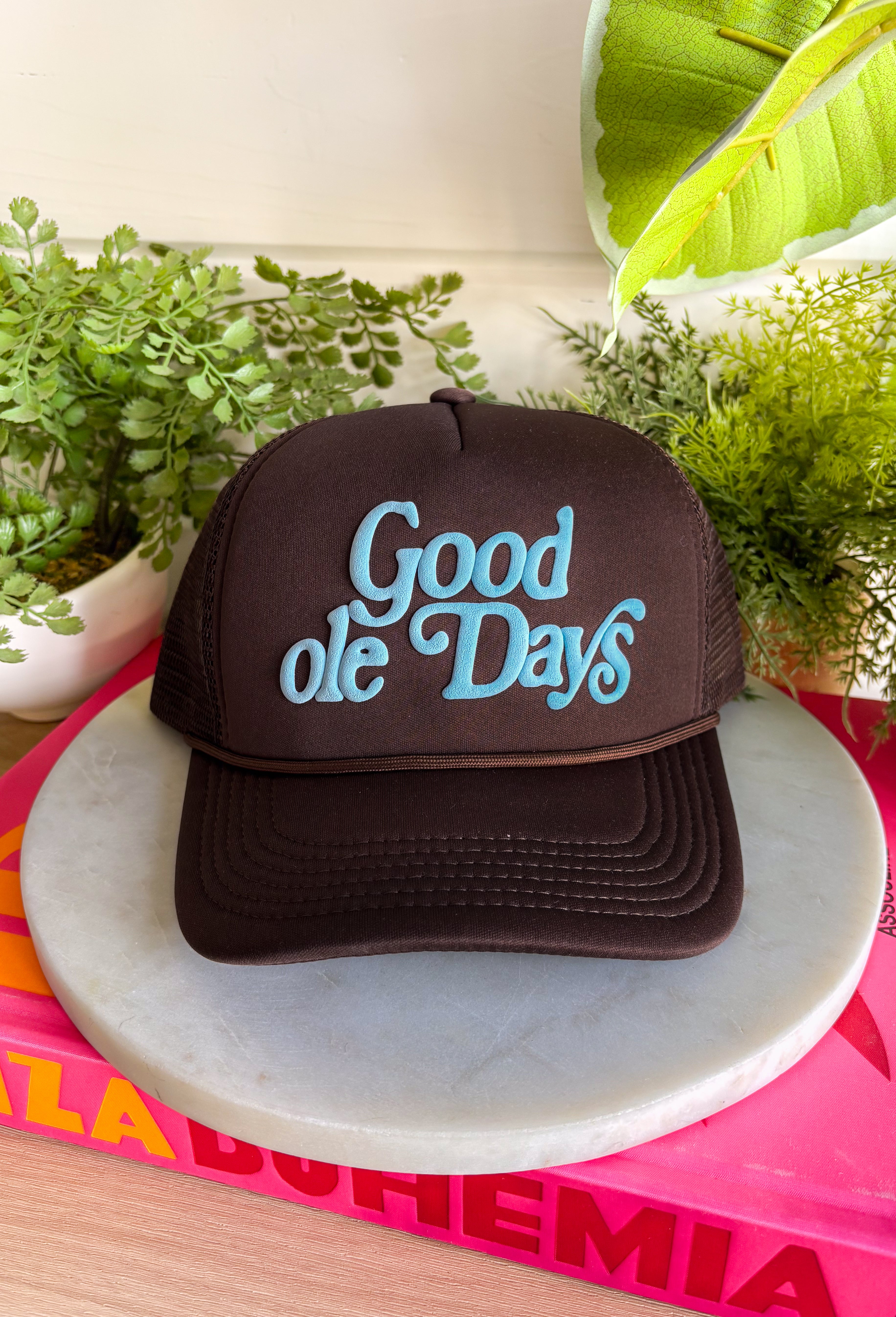 A little nostalgic and a whole lot cute! This brown trucker hat features “Good Ole Days” in a soft light blue, giving it that easy, throwback charm. The neutral brown paired with the pop of blue makes it effortless to style while still adding personality to your everyday look.&nbsp;With a classic mesh backing for breathability and an adjustable fit, this one is perfect for concerts, road trips, or just soaking up slow, sweet moments. It’s the kind of hat that feels timeless from the very first wear.