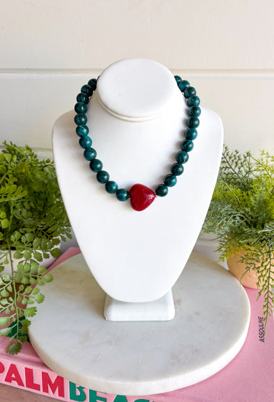 Rich seasonal color makes this beaded necklace a fun addition to your fall-to-winter jewelry lineup. Teal beads create a bold, colorful base, while the burgundy sideways heart adds a warm contrast at the front. The mix of deep teal and burgundy feels especially fitting for cooler weather and adds an easy pop of color to cozy sweaters, dresses, and holiday-season outfits. Wear it on its own for a playful statement or layer it with simple gold chains for a little extra shine.