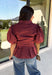 Rich burgundy and pretty shaping details make this top from Entro an easy pick for fall. The button-front design keeps the look classic, while a pleated waist and self-tie detail create a flattering shape that gives the silhouette a little something extra. Short puff sleeves add soft volume and balance out the fitted waist beautifully. Made from a cotton-blend fabric with a touch of stretch, it’s comfortable enough for all-day wear while still looking put together. 