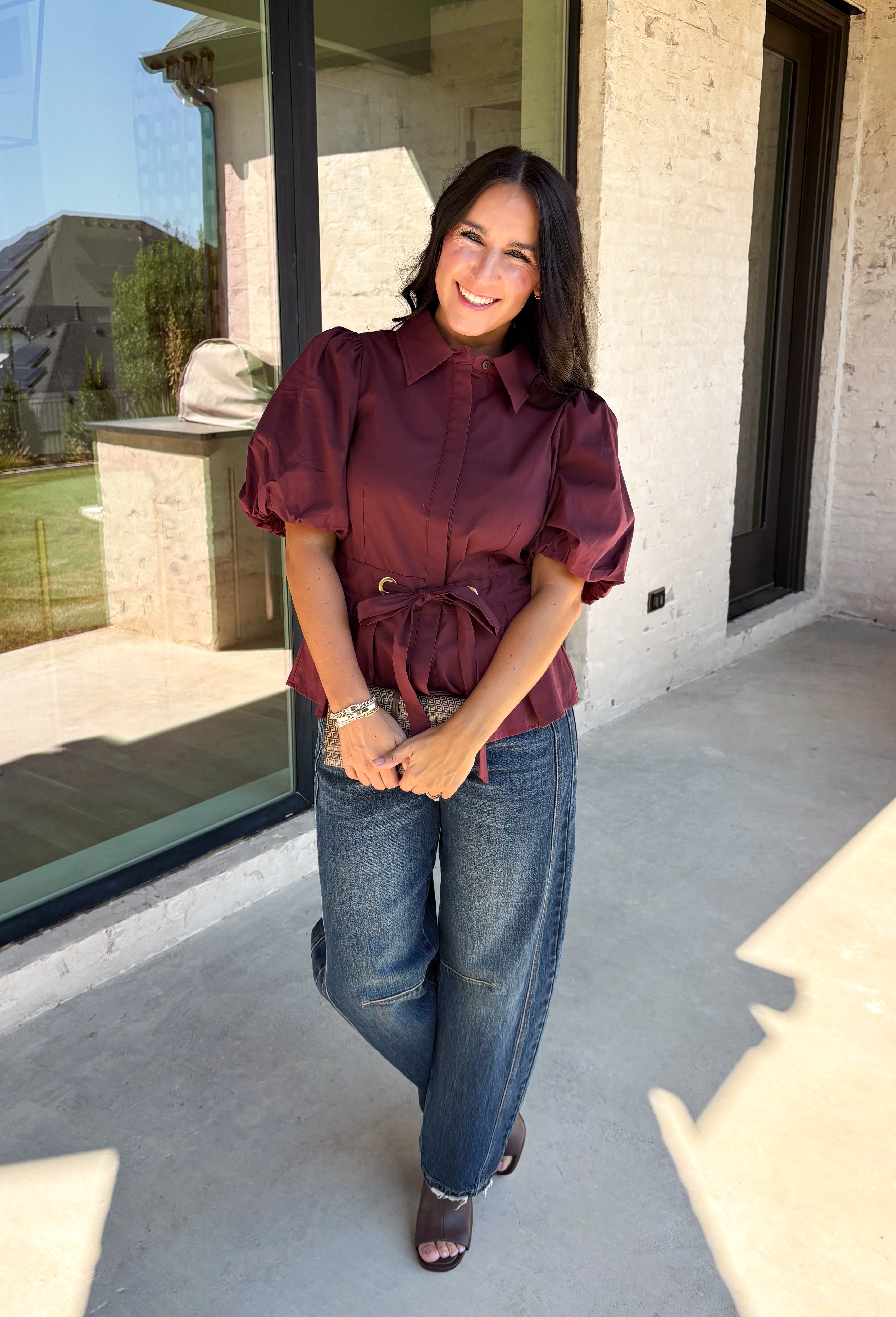 Rich burgundy and pretty shaping details make this top from Entro an easy pick for fall. The button-front design keeps the look classic, while a pleated waist and self-tie detail create a flattering shape that gives the silhouette a little something extra. Short puff sleeves add soft volume and balance out the fitted waist beautifully. Made from a cotton-blend fabric with a touch of stretch, it’s comfortable enough for all-day wear while still looking put together. 