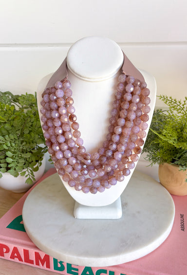 Add a pretty pop of purple to your look with this eye-catching layered beaded necklace. Featuring seven strands of light purple beads, this chunky statement piece creates a full, dimensional look that makes even the simplest outfit feel a little more fun. The faux leather backing helps keep each layer beautifully arranged, while the magnetic closure makes it easy to put on and take off. It’s the perfect finishing touch for sweaters, dresses, blouses, and everyday basics.