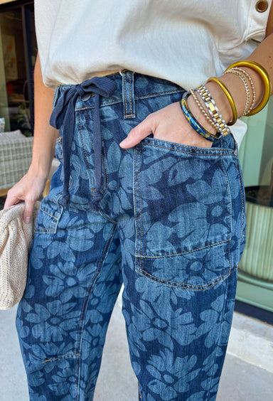 These dark wash barrel jeans bring a fresh, modern twist to everyday denim with a subtle monochromatic floral print woven throughout. The medium wash floral design adds just enough texture and interest while keeping the look sleek and easy to style. Finished with a tie detail at the waist, these jeans offer an adjustable, comfortable fit that still feels polished. The barrel-leg silhouette gives them that relaxed, on-trend shape that pairs perfectly with everything from fitted tees to flowy spring tops.