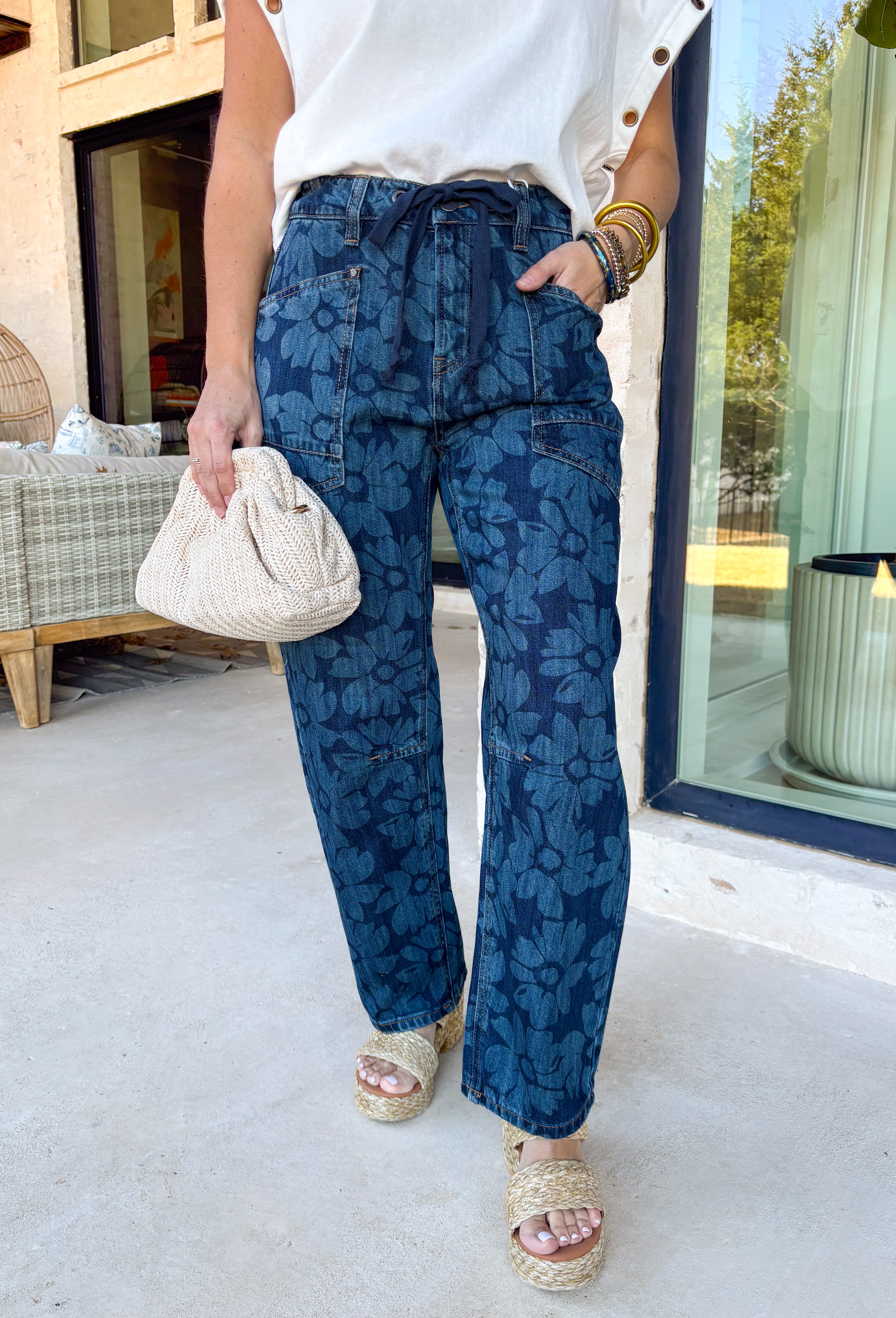 These dark wash barrel jeans bring a fresh, modern twist to everyday denim with a subtle monochromatic floral print woven throughout. The medium wash floral design adds just enough texture and interest while keeping the look sleek and easy to style. Finished with a tie detail at the waist, these jeans offer an adjustable, comfortable fit that still feels polished. The barrel-leg silhouette gives them that relaxed, on-trend shape that pairs perfectly with everything from fitted tees to flowy spring tops.