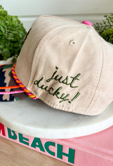 Add a playful outdoor-inspired touch to your everyday look with this unique trucker hat. Featuring a neutral faux suede front and a camouflage bill, this standout style is embroidered with a detailed mallard design accented by pink and orange stitching for an unexpected pop of color. The side is embroidered with "Just Ducky," while the back features "It's A Good Life" in olive green, giving this hat personality from every angle. 