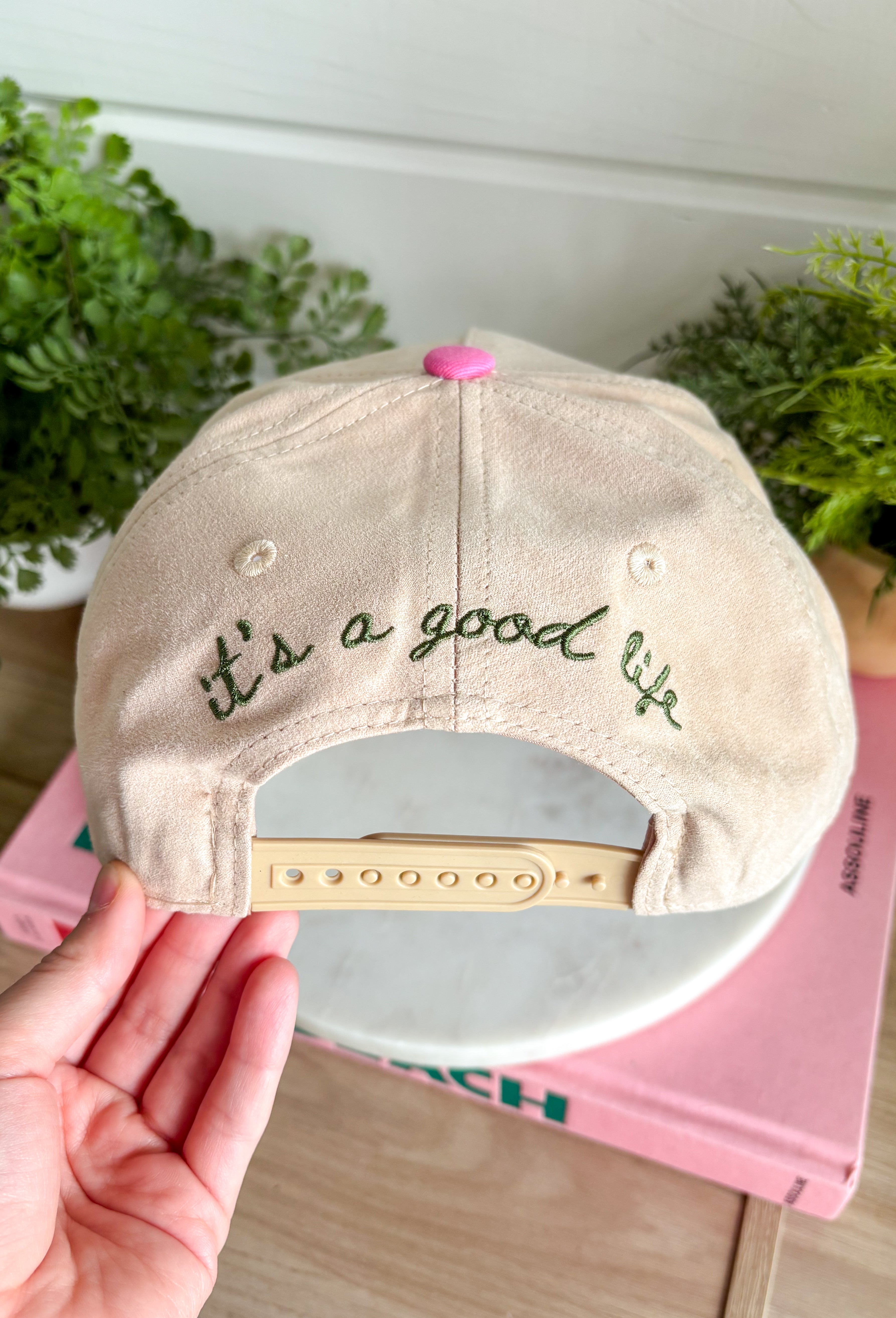 Add a playful outdoor-inspired touch to your everyday look with this unique trucker hat. Featuring a neutral faux suede front and a camouflage bill, this standout style is embroidered with a detailed mallard design accented by pink and orange stitching for an unexpected pop of color. The side is embroidered with "Just Ducky," while the back features "It's A Good Life" in olive green, giving this hat personality from every angle. 
