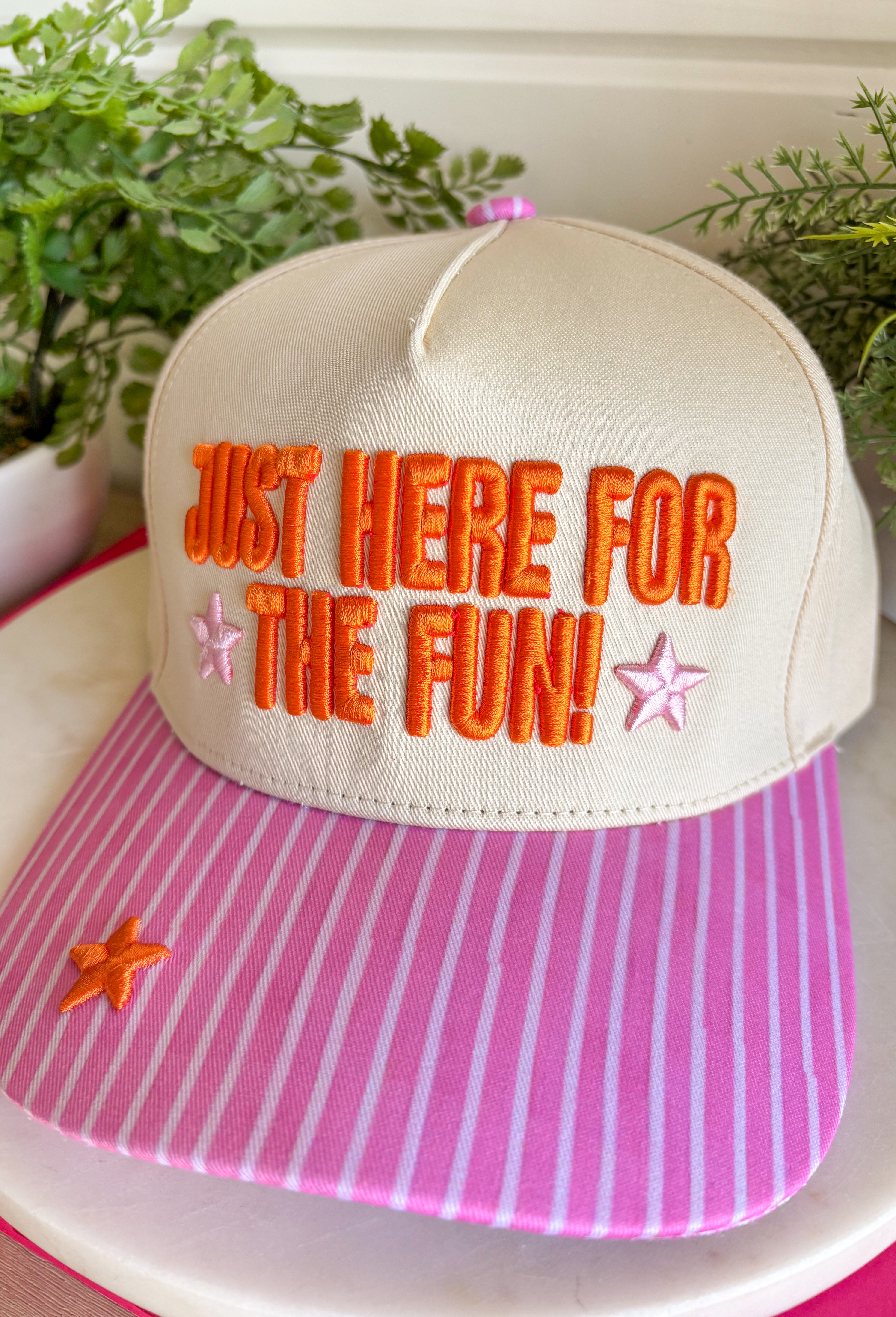 Bring a little extra fun wherever you go with this playful trucker hat! Featuring "Just Here For The Fun" embroidered in bright orange, this hat is made for football Saturdays, fall festivals, road trips, and spontaneous adventures. The pink bill with neutral stripes adds the perfect pop of color, while the light pink and orange embroidered stars give it a cheerful finishing touch. 