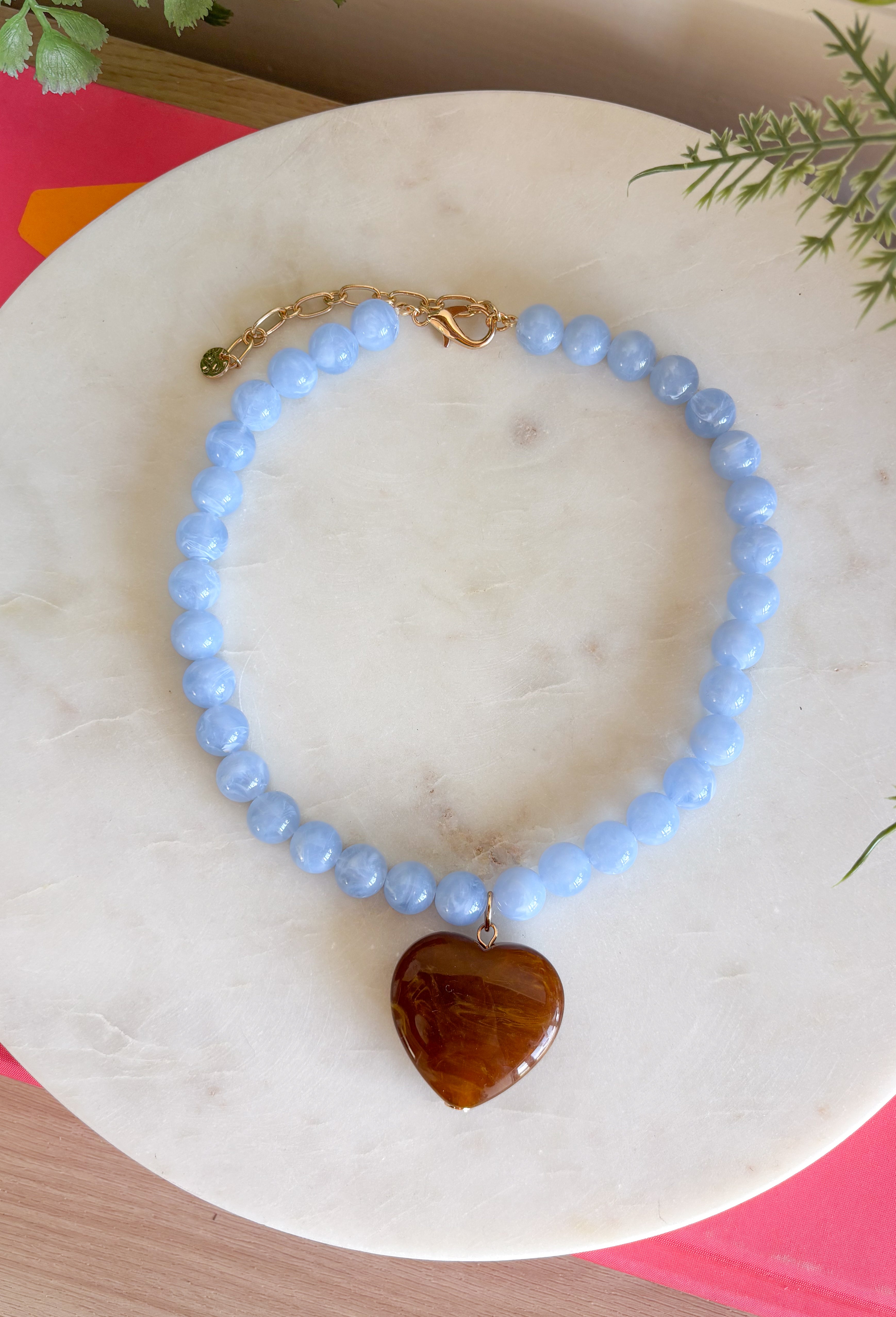 Fun, playful, and full of personality! This necklace features light blue beading paired with a brown heart pendant for the perfect touch of contrast. Lightweight and easy to style, this necklace looks just as cute worn on its own as it does layered with your favorite chains and beaded pieces. It’s the perfect finishing touch for adding a subtle pop of color to your everyday outfits.