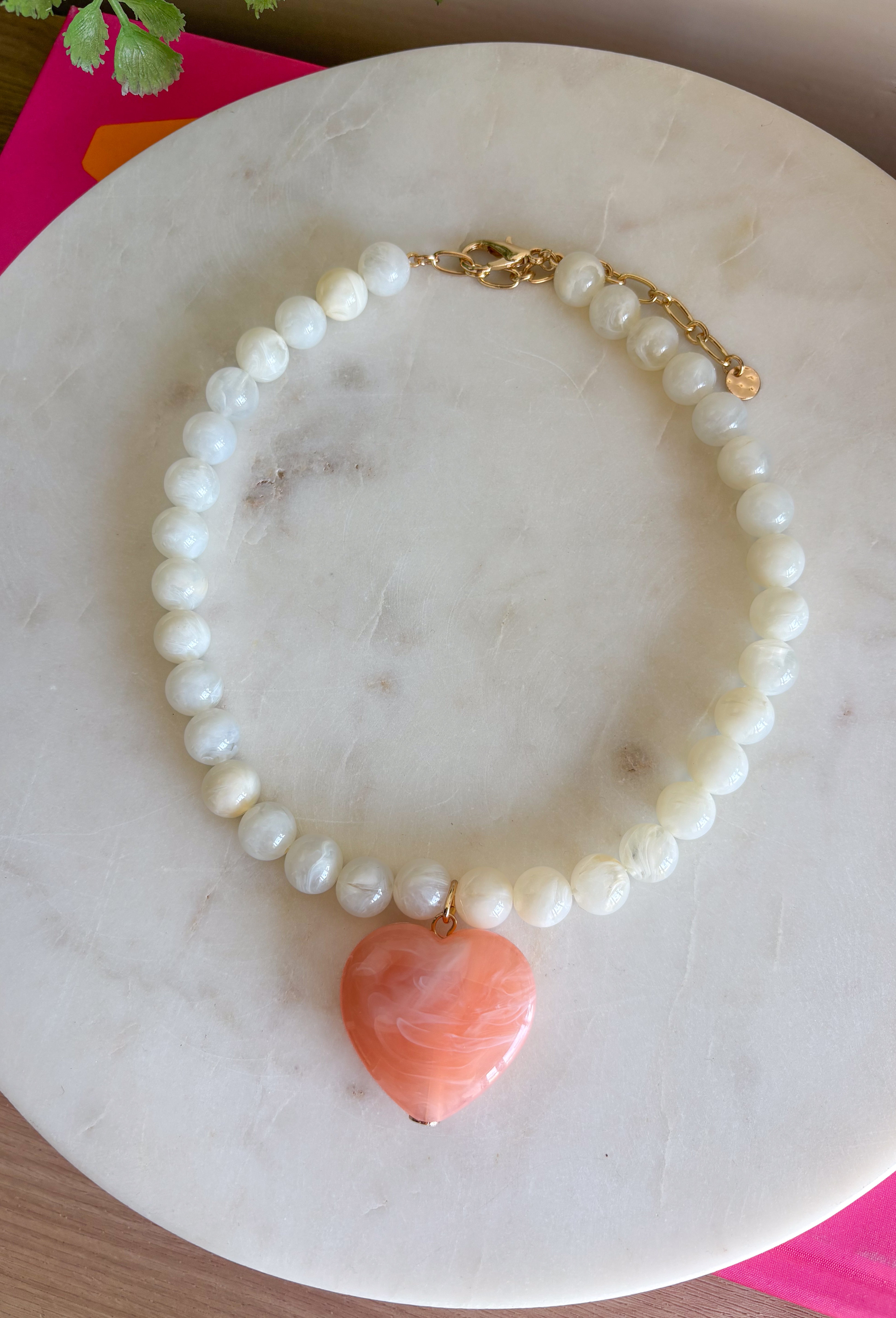 Sweet, playful, and full of charm! This white beaded necklace features a light pink heart pendant that adds the perfect soft pop of color. The combination of crisp white beads and the blush heart charm creates a fresh, feminine look that’s easy to style for everyday wear. Lightweight and easy to layer, this necklace looks just as cute worn on its own as it does stacked with your favorite gold or beaded pieces. It’s a simple way to add a little love and personality to any outfit.