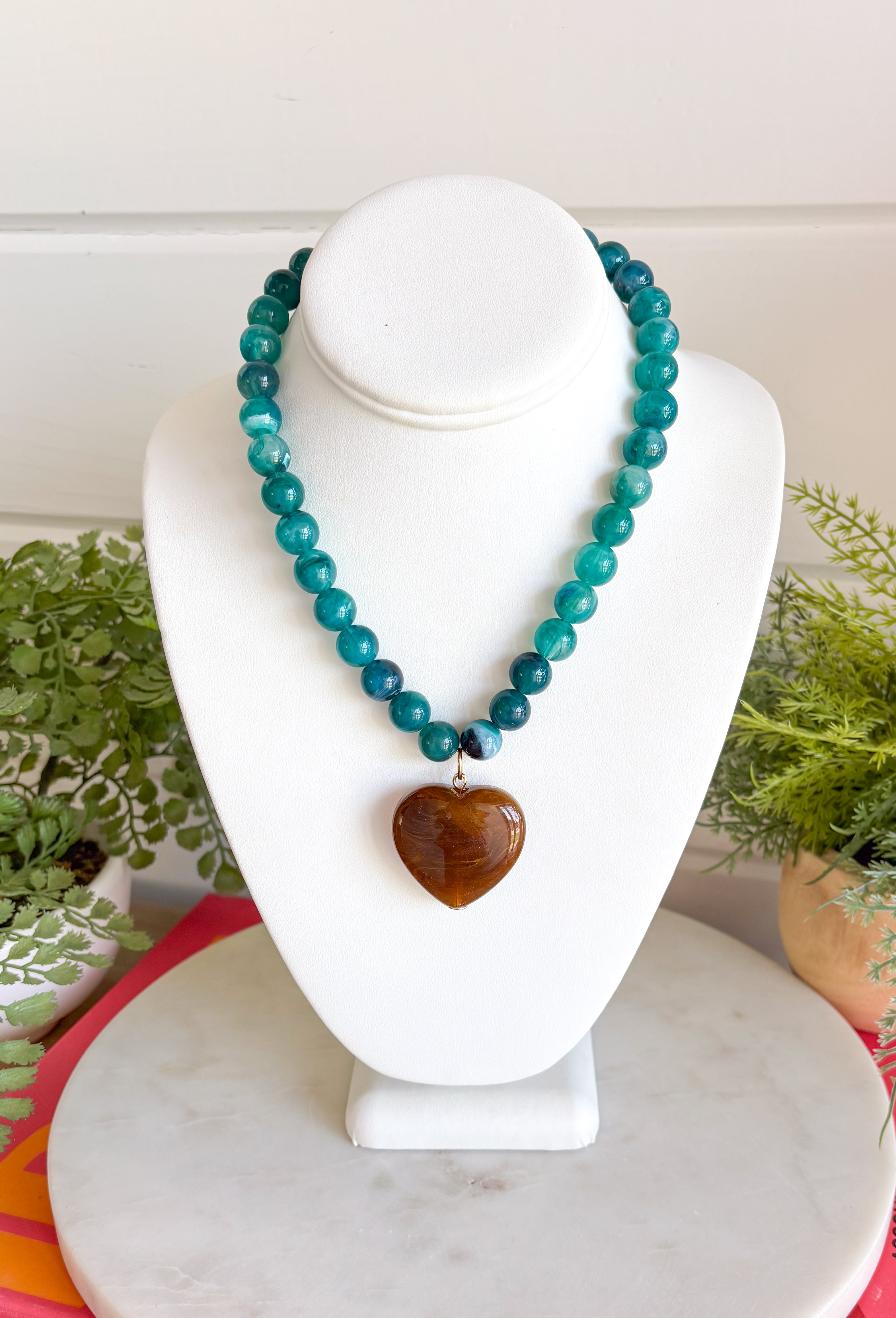 Fun, playful, and full of personality!&nbsp;This necklace features teal beading paired with a brown heart pendant for the perfect touch of contrast. Lightweight and easy to style, this necklace looks just as cute worn on its own as it does layered with your favorite chains and beaded pieces. It’s the perfect finishing touch for adding a subtle pop of color to your everyday outfits.