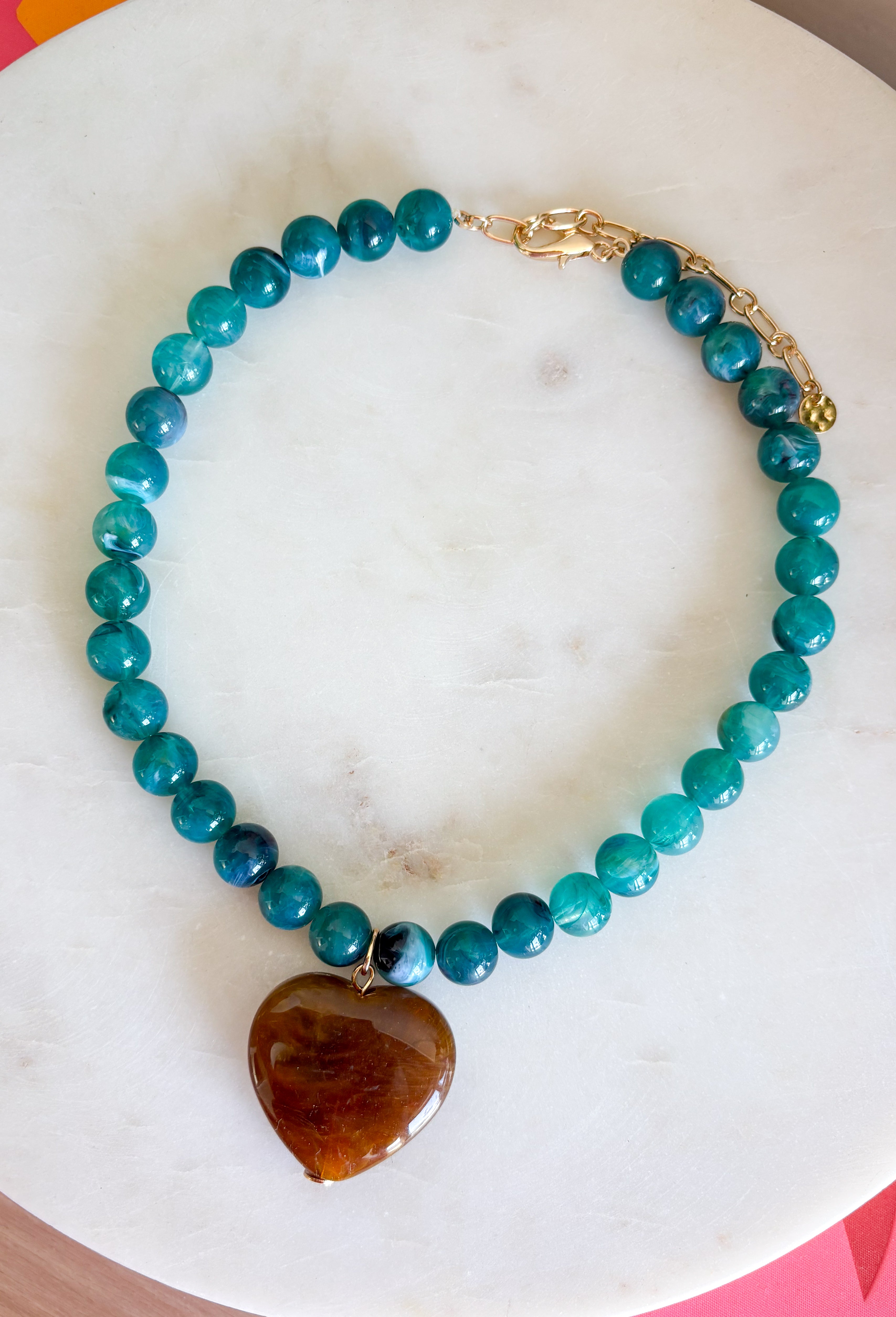 Fun, playful, and full of personality!&nbsp;This necklace features teal beading paired with a brown heart pendant for the perfect touch of contrast. Lightweight and easy to style, this necklace looks just as cute worn on its own as it does layered with your favorite chains and beaded pieces. It’s the perfect finishing touch for adding a subtle pop of color to your everyday outfits.